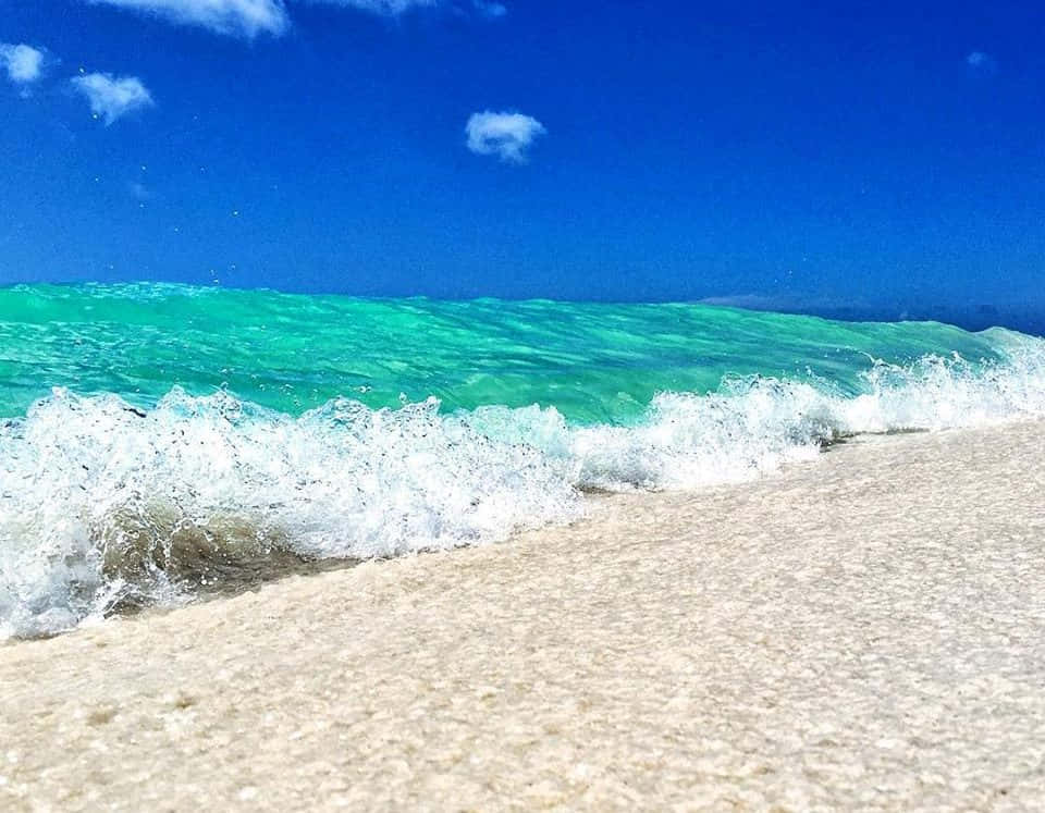 阿魯巴海灘浪花特寫照片 壁紙 — 清澈的碧綠色海浪拍打著粉狀白色沙灘，上方是藍天白雲。