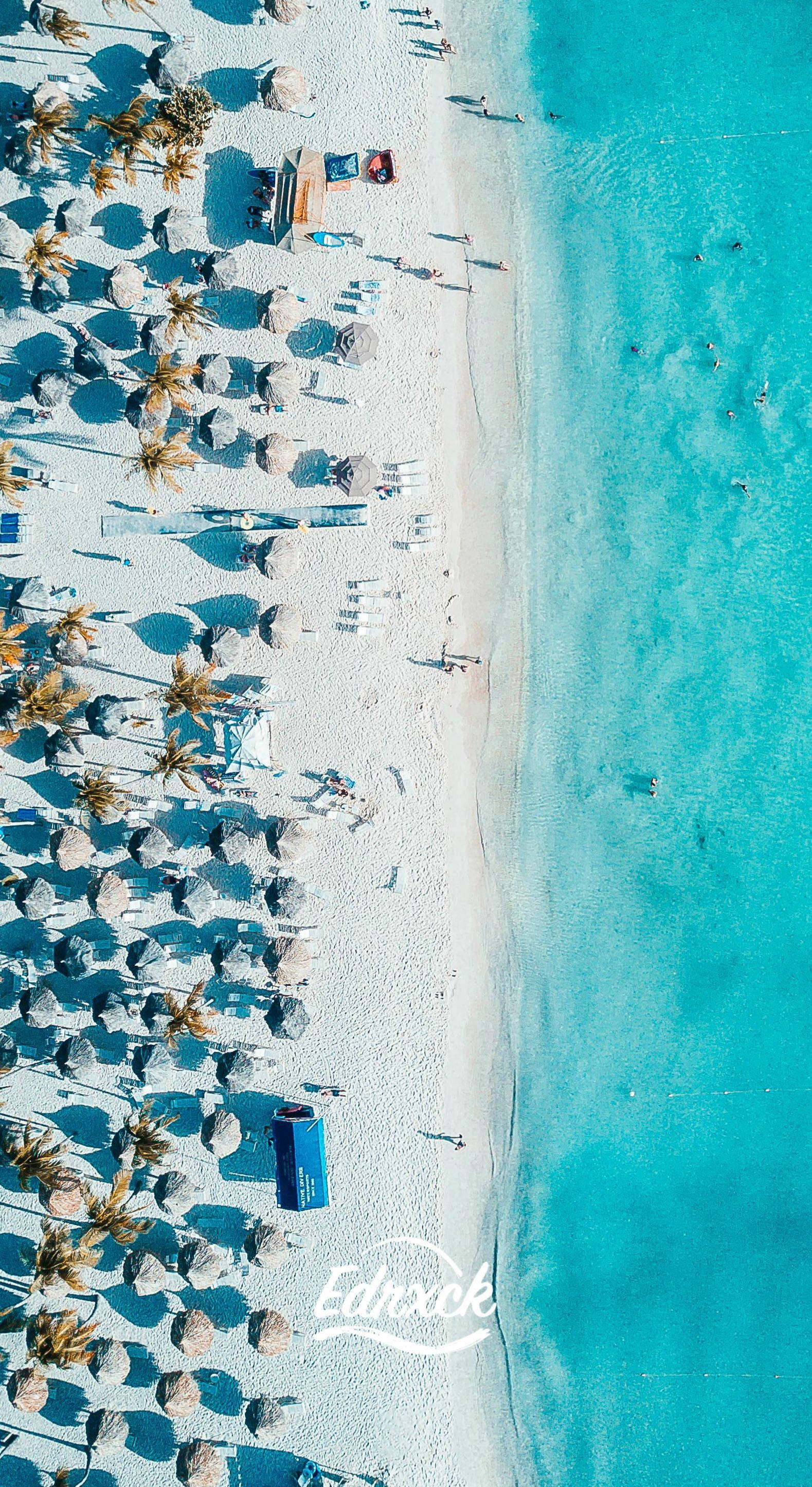 阿魯巴海灘無人機俯瞰 壁紙 — 原始熱帶海灘的鳥瞰圖，碧綠的海水，一排排茅草傘投下長長的影子。