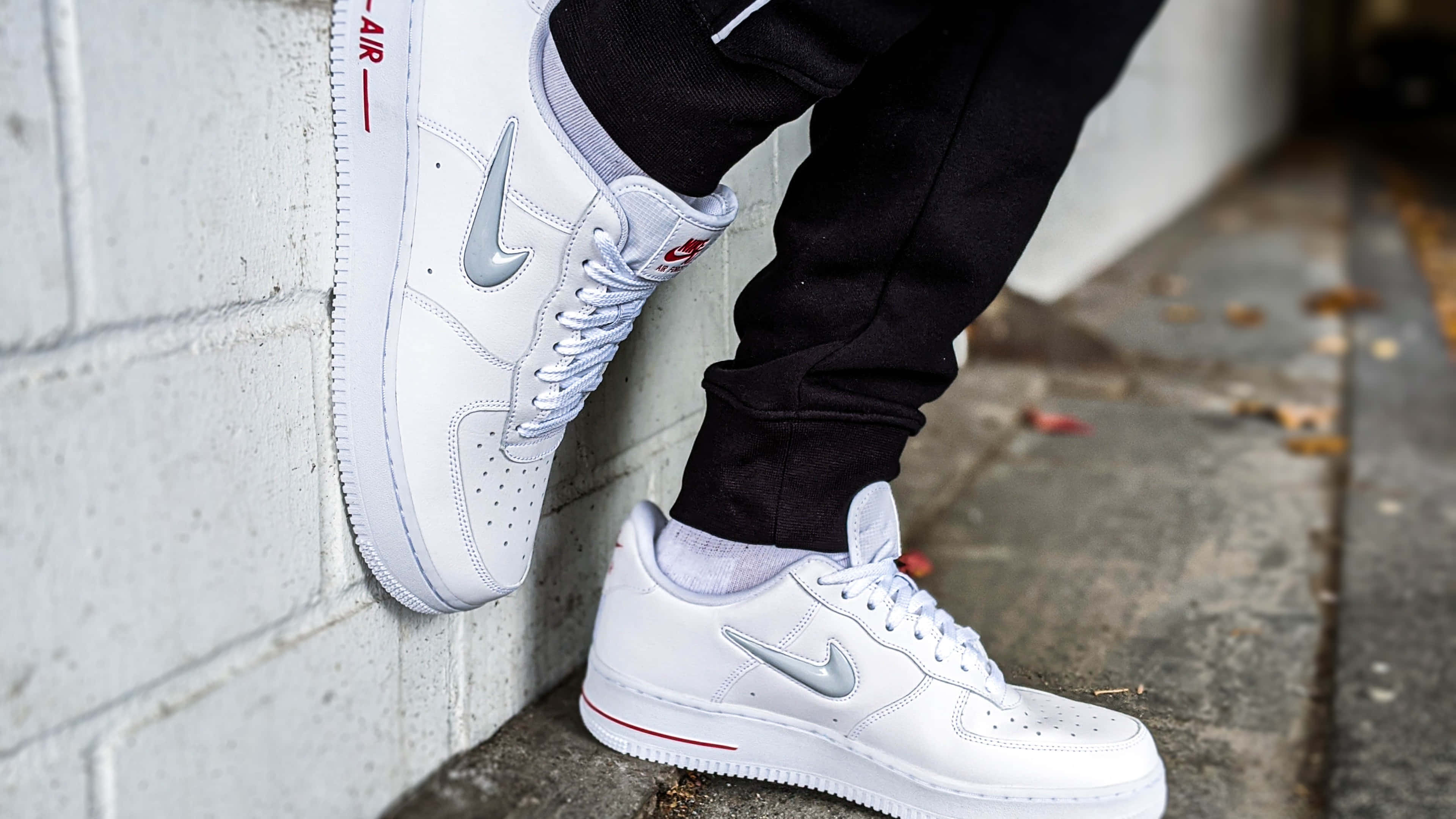 限量版 Jordan 鞋 4K 鞋款 壁紙 — 白色Nike Air Force 1波鞋特寫，帶有銀色swoosh和紅色點綴，由靠著混凝土牆的人穿著。