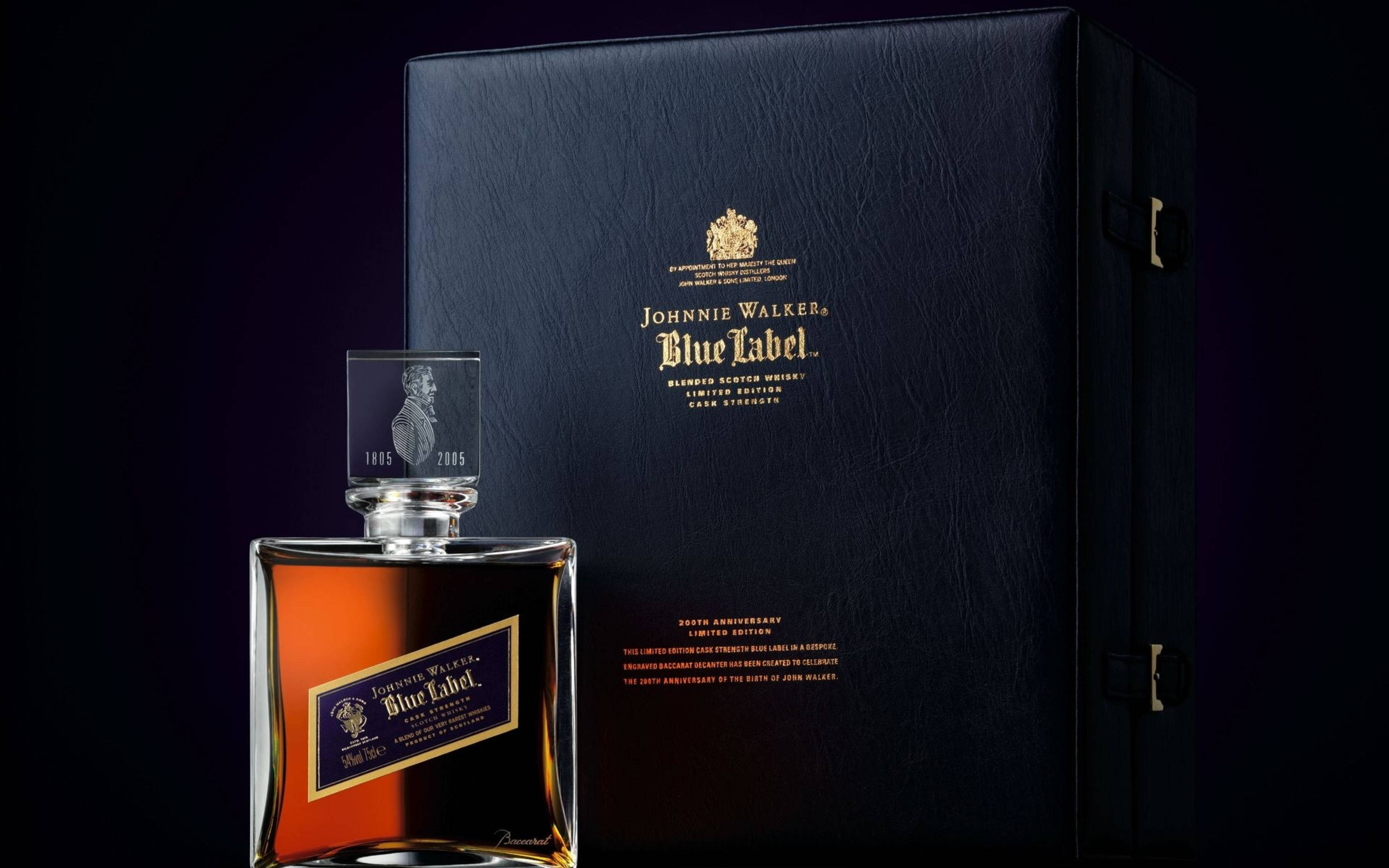 限量版藍標尊尼獲加威士忌 壁紙 — 一瓶奢華的Johnnie Walker Blue Label威士忌在戲劇性的工作室燈光下，在其優雅的黑色禮盒旁閃閃發光。