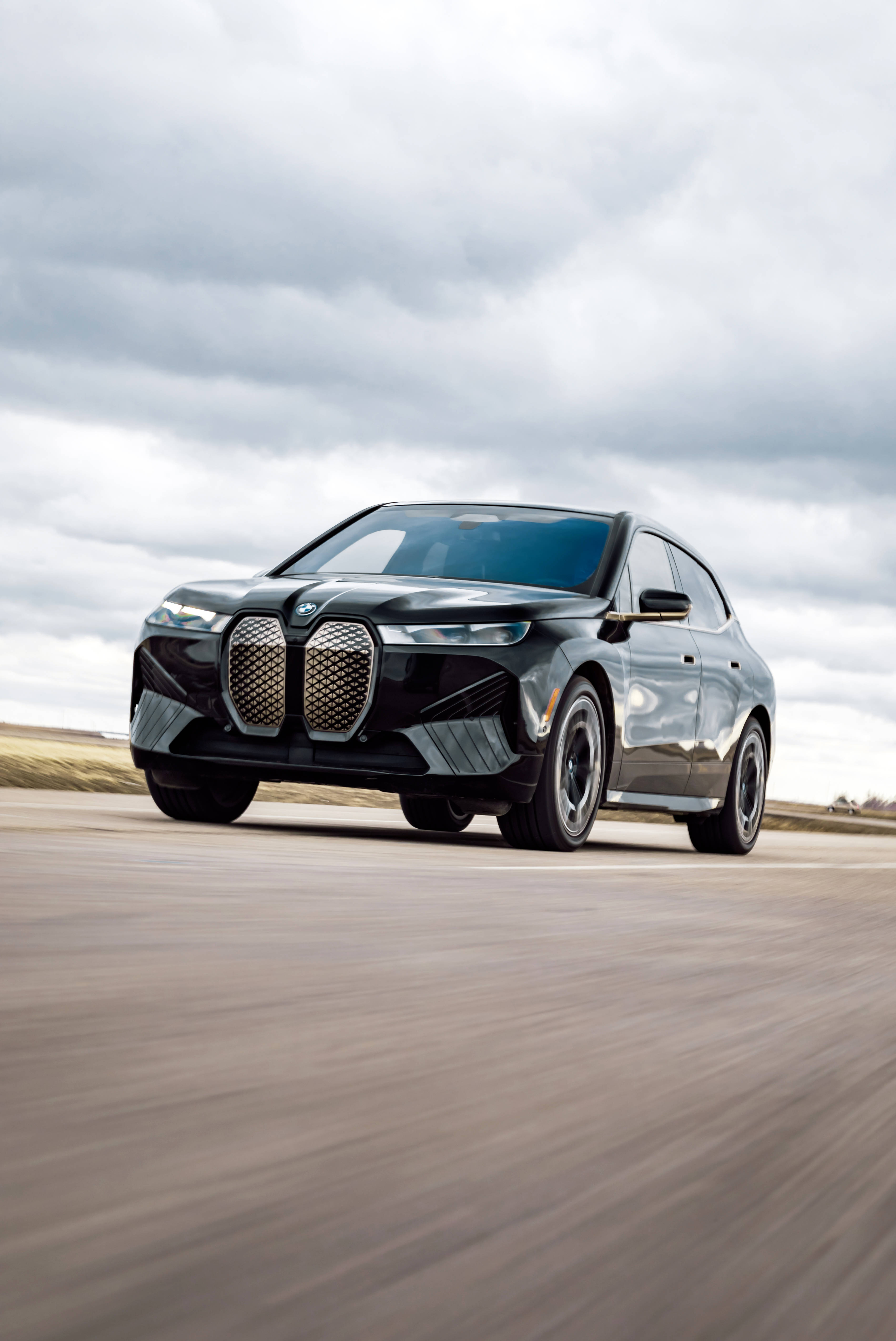 陰天行駛的黑色BMW M 壁紙 — 一輛時尚的黑色BMW iX電動SUV在陰天下一條模糊的沙漠公路上疾馳。