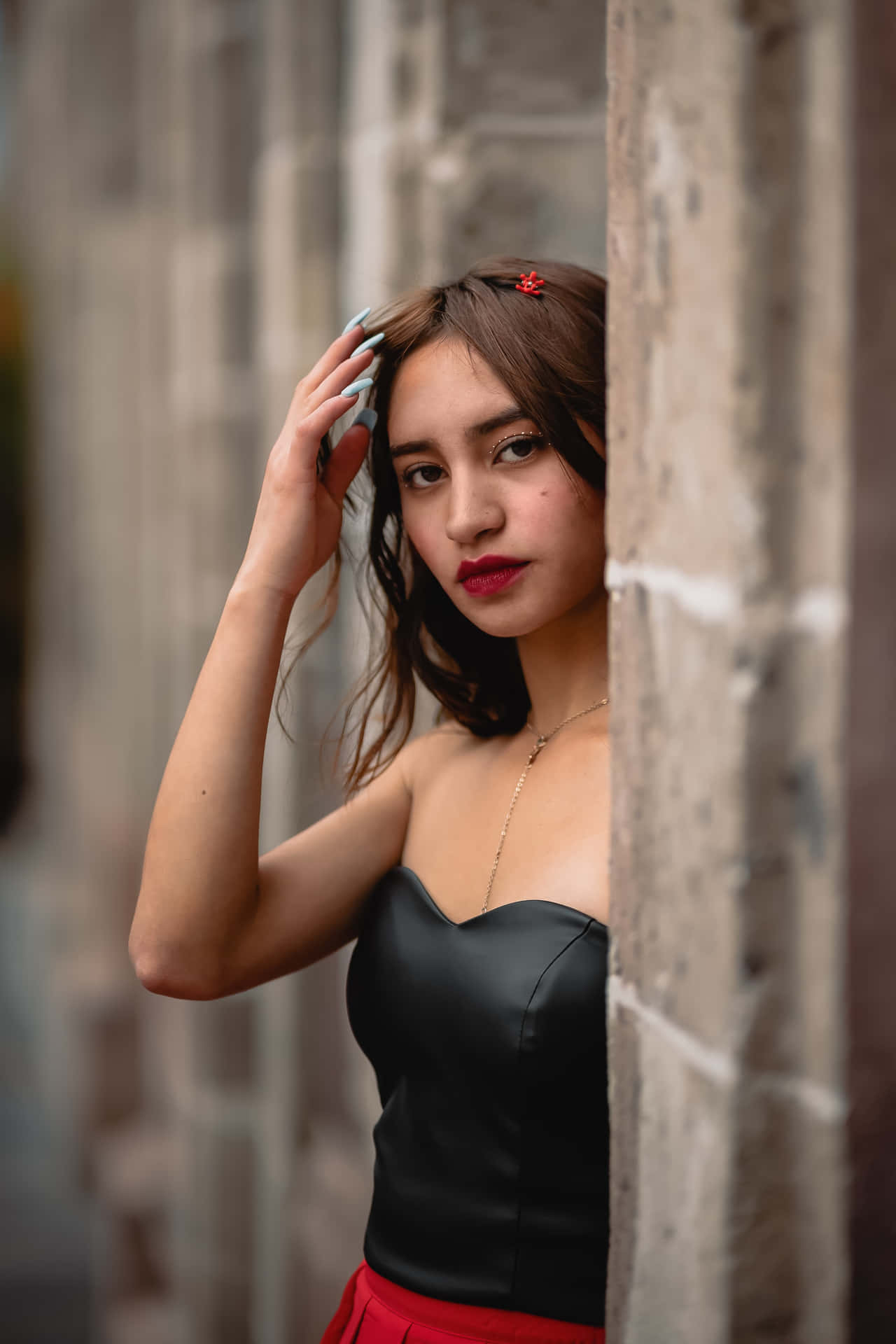 年輕女子從石牆後探出頭來，身穿黑色上衣和紅色裙子。