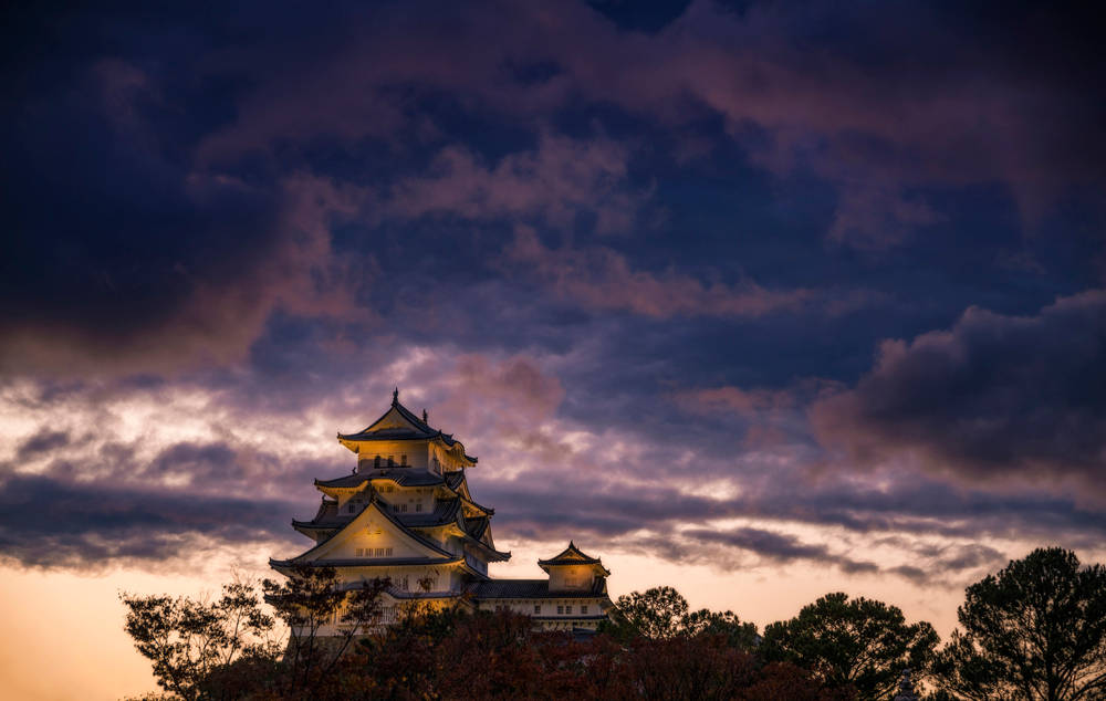 一座日本城堡在暮色中亮起，上方有彩色雲朵。