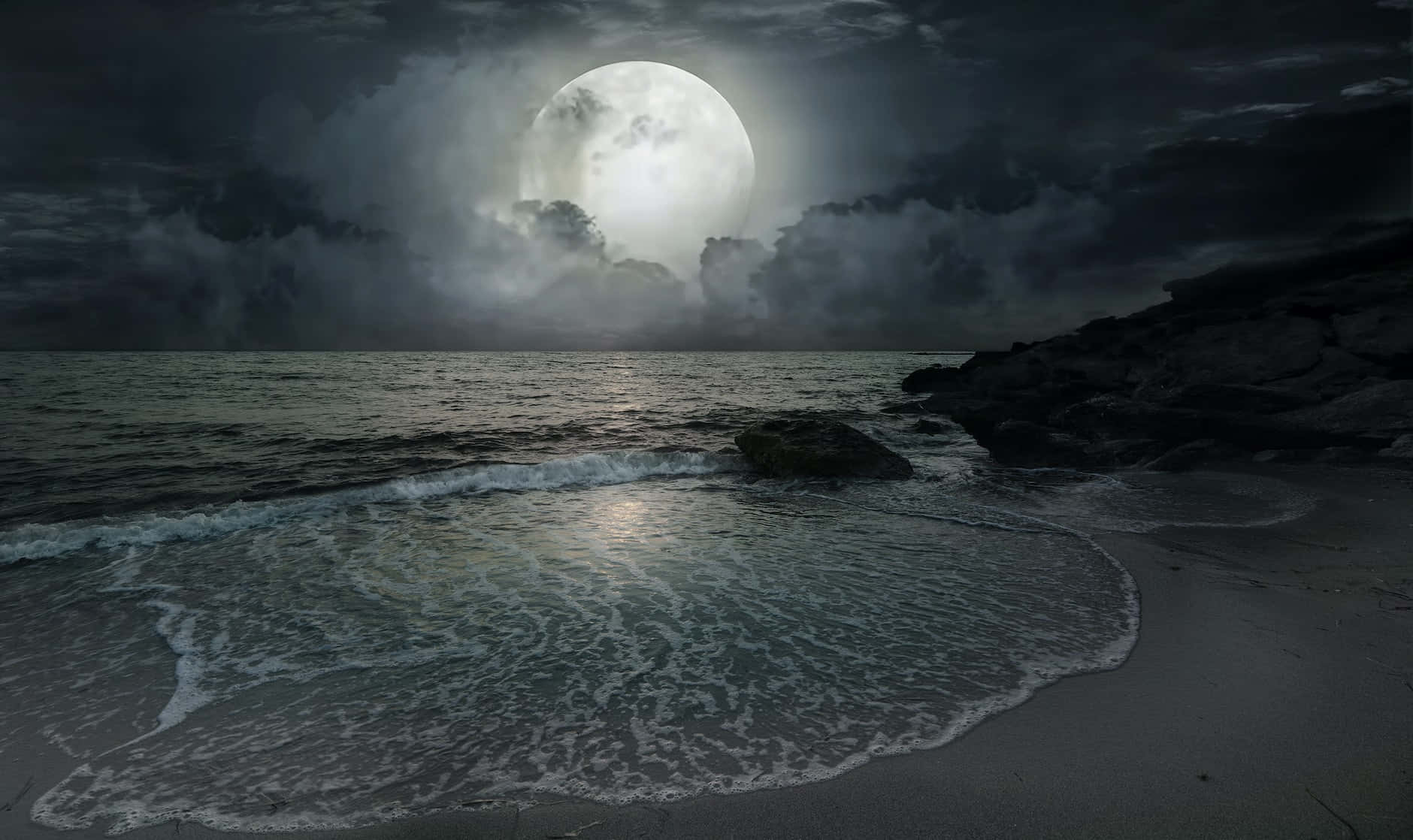 月光下的海浪在暴風雨的夜空下拍打著岩石海灘。