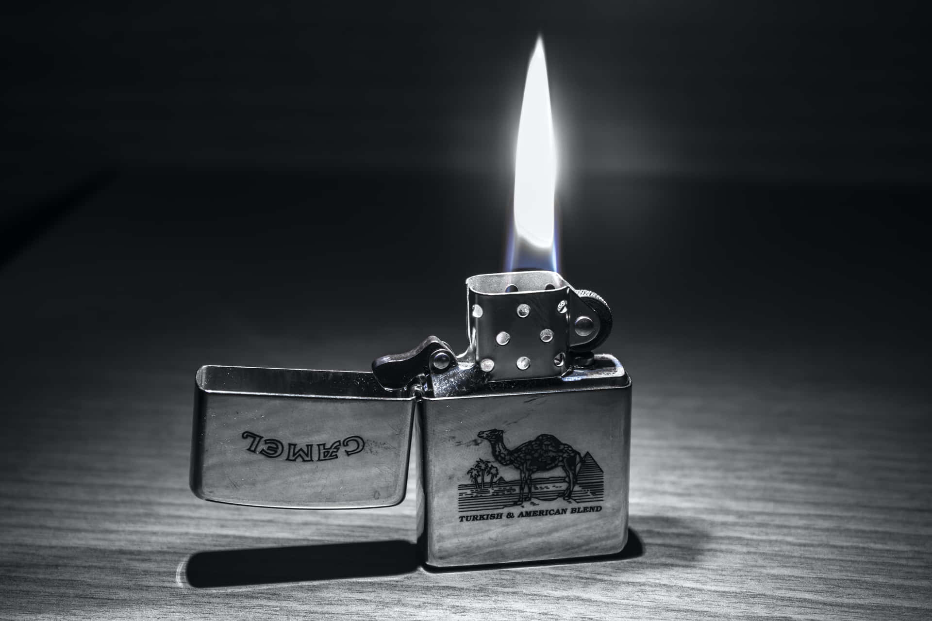 一個點燃的Camel品牌打火機放在木桌上，帶有戲劇性的燈光效果。
