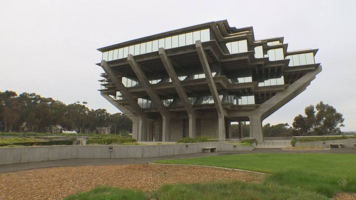 陰鬱 UCSD 壁紙 — 一座引人注目的粗獷主義混凝土建築，帶有分層玻璃陽台，矗立在陰天之下，周圍是修剪整齊的草坪和樹木。