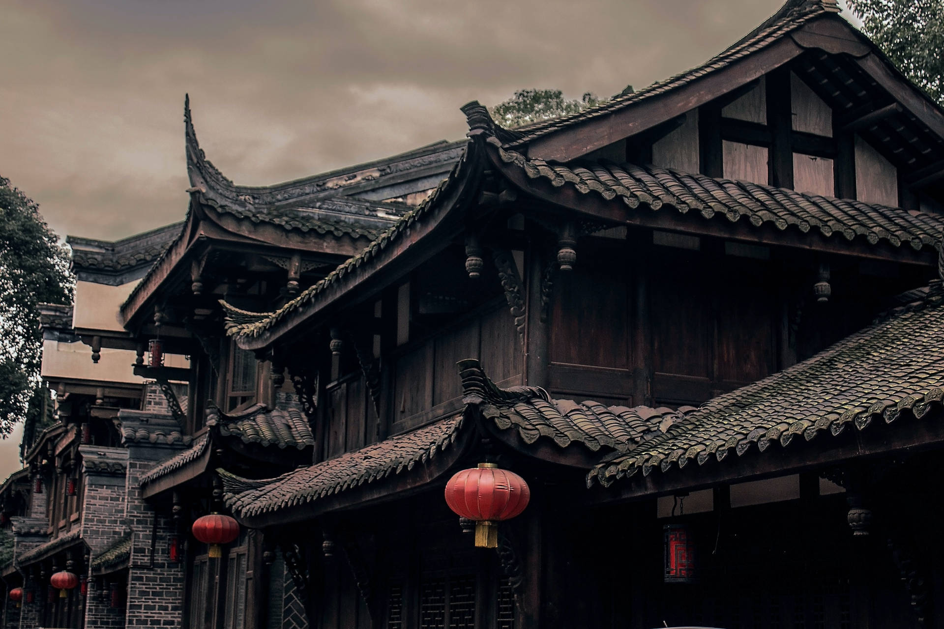 多雲天空下，掛著紅色燈籠的古老中式木建築。