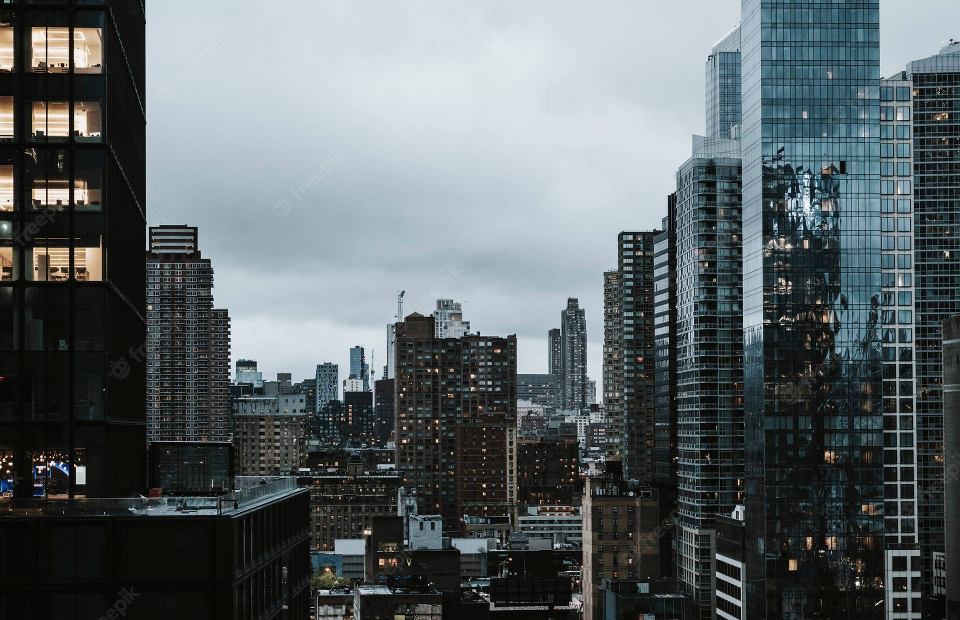多雲天空下，高聳玻璃建築和發光窗戶的黃昏城市景觀。