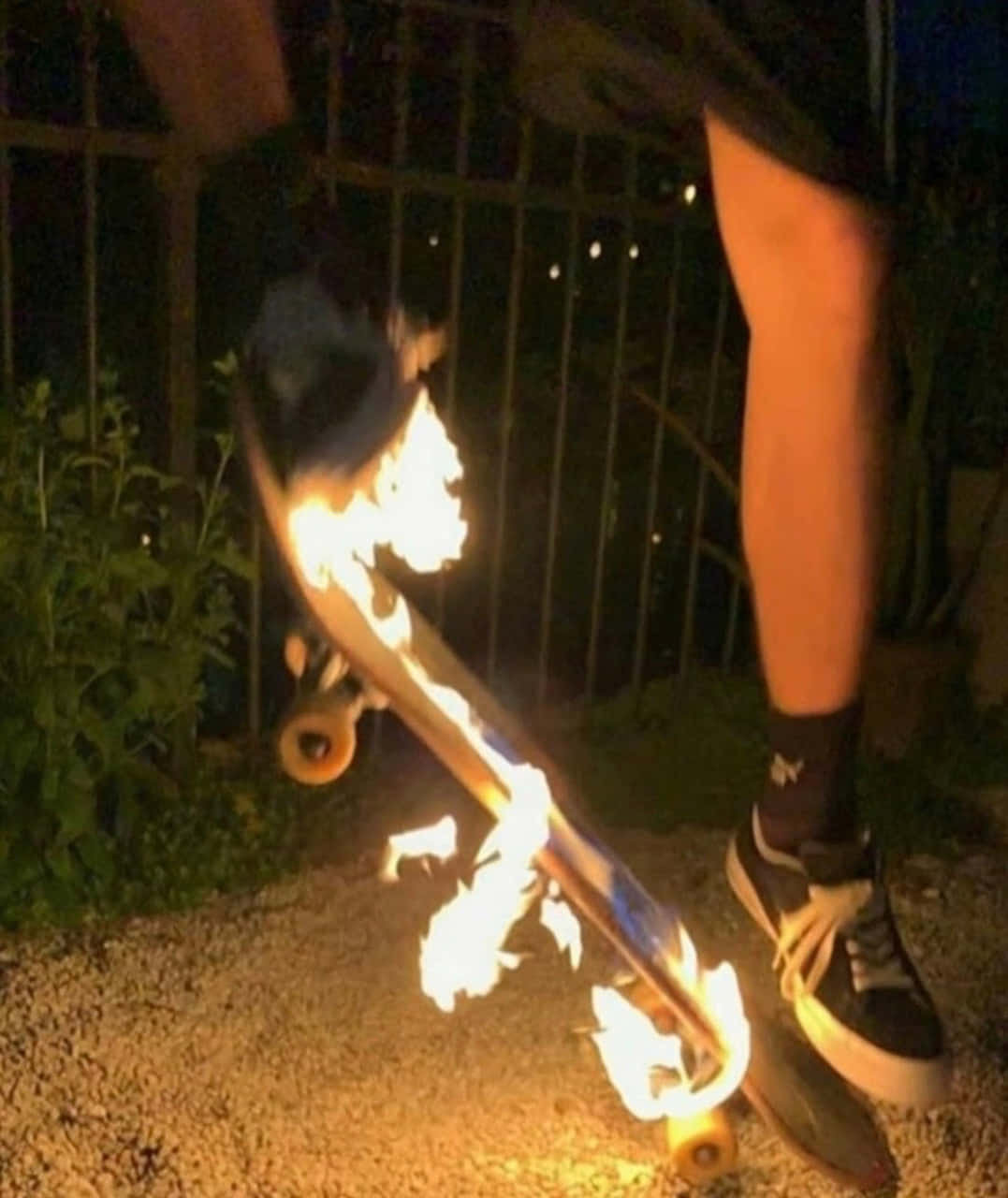 夜間手持一塊燃燒的滑板，附近有人的腳。