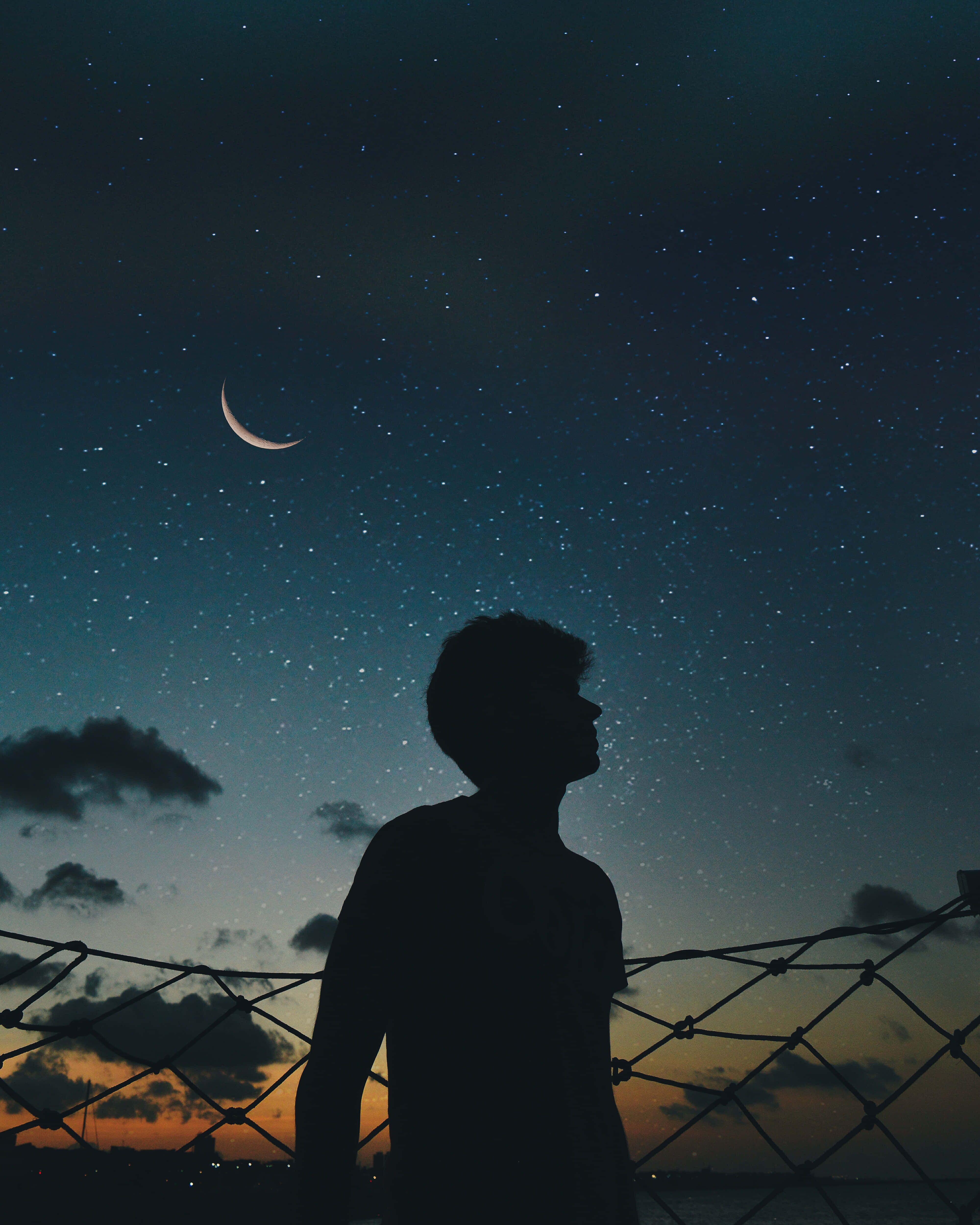 陰鬱的天空 壁紙 — 一個人的剪影仰望鐵絲網上方的彎月和星空。