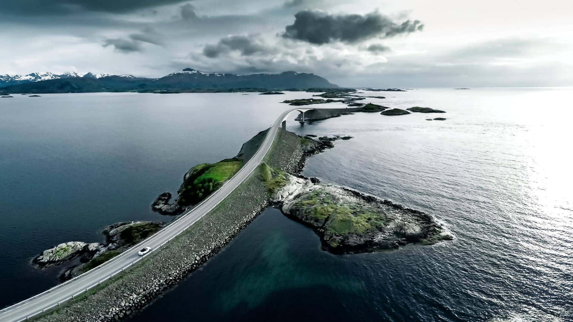 一輛孤獨的汽車沿著連接岩石島嶼的海岸公路行駛，呈現戲劇性的海景。
