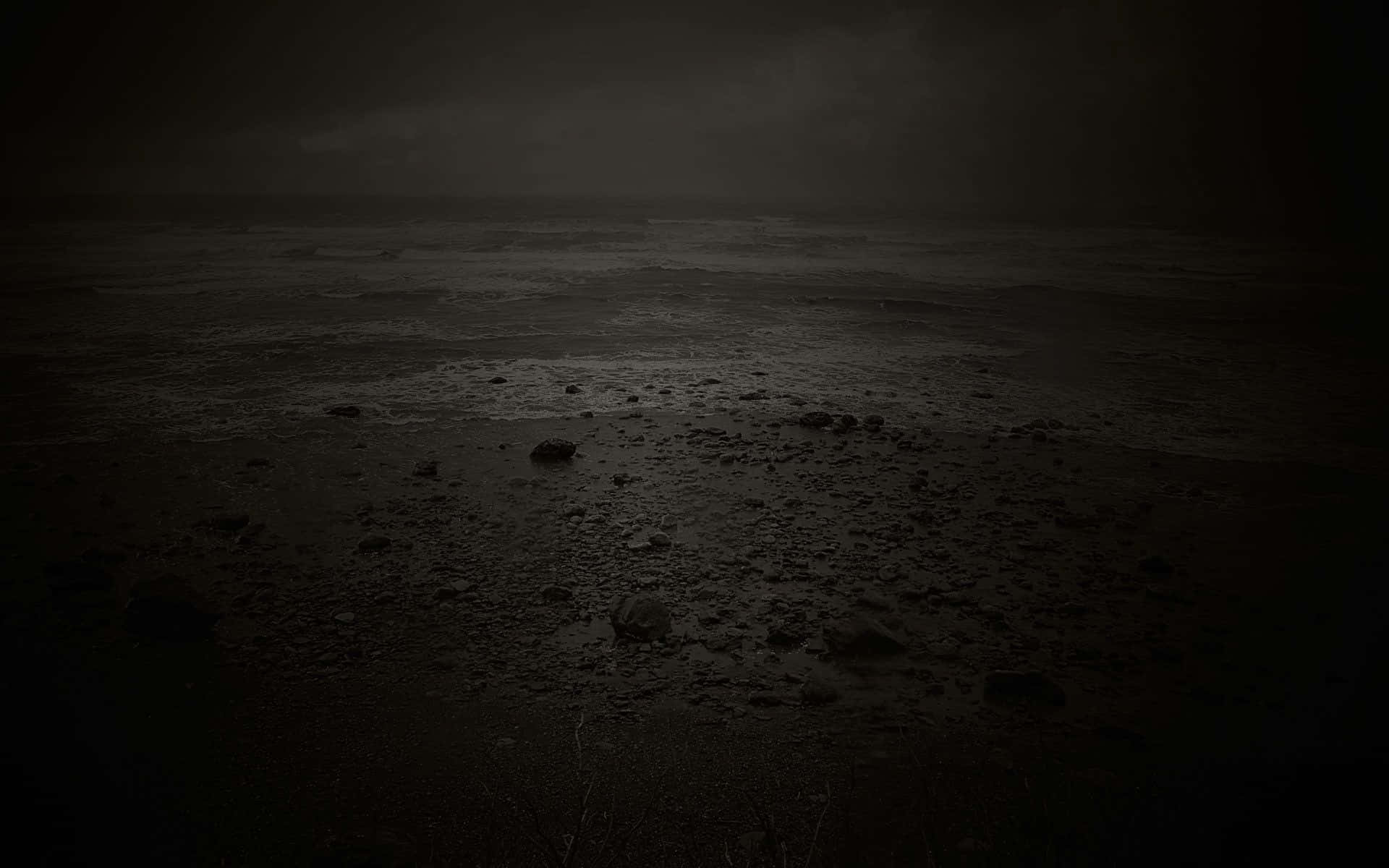 夜晚陰暗暴風雨的海灘，濕沙和散落的岩石。