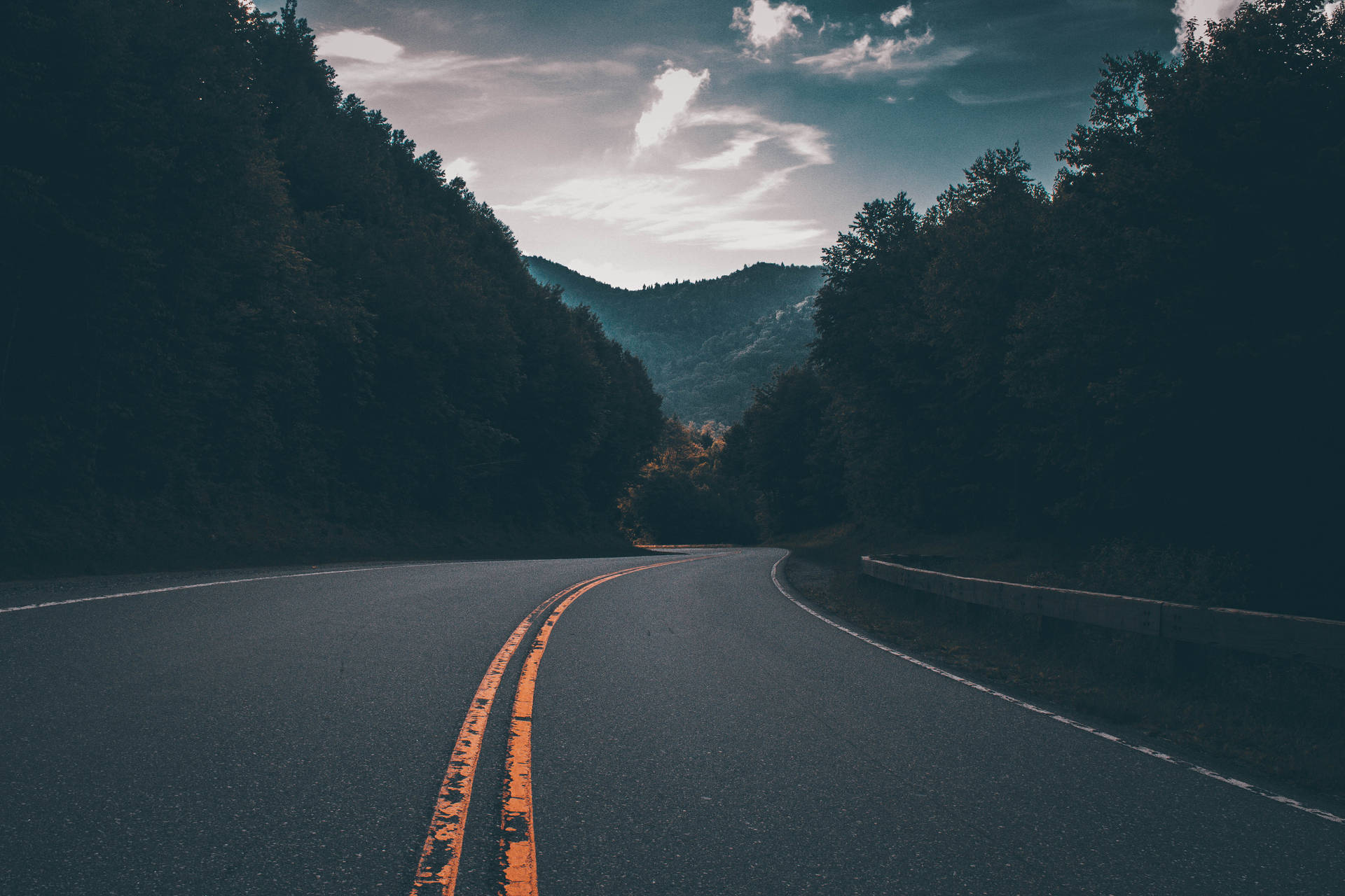 暮色天空下山脈森林中的蜿蜒道路