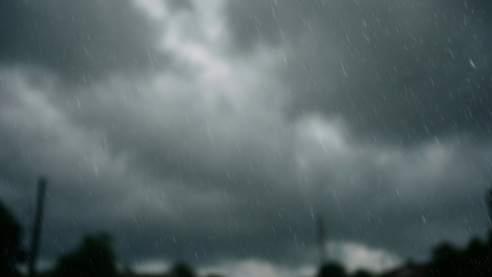 黑暗的暴風雲伴隨大雨落在模糊的樹木剪影上