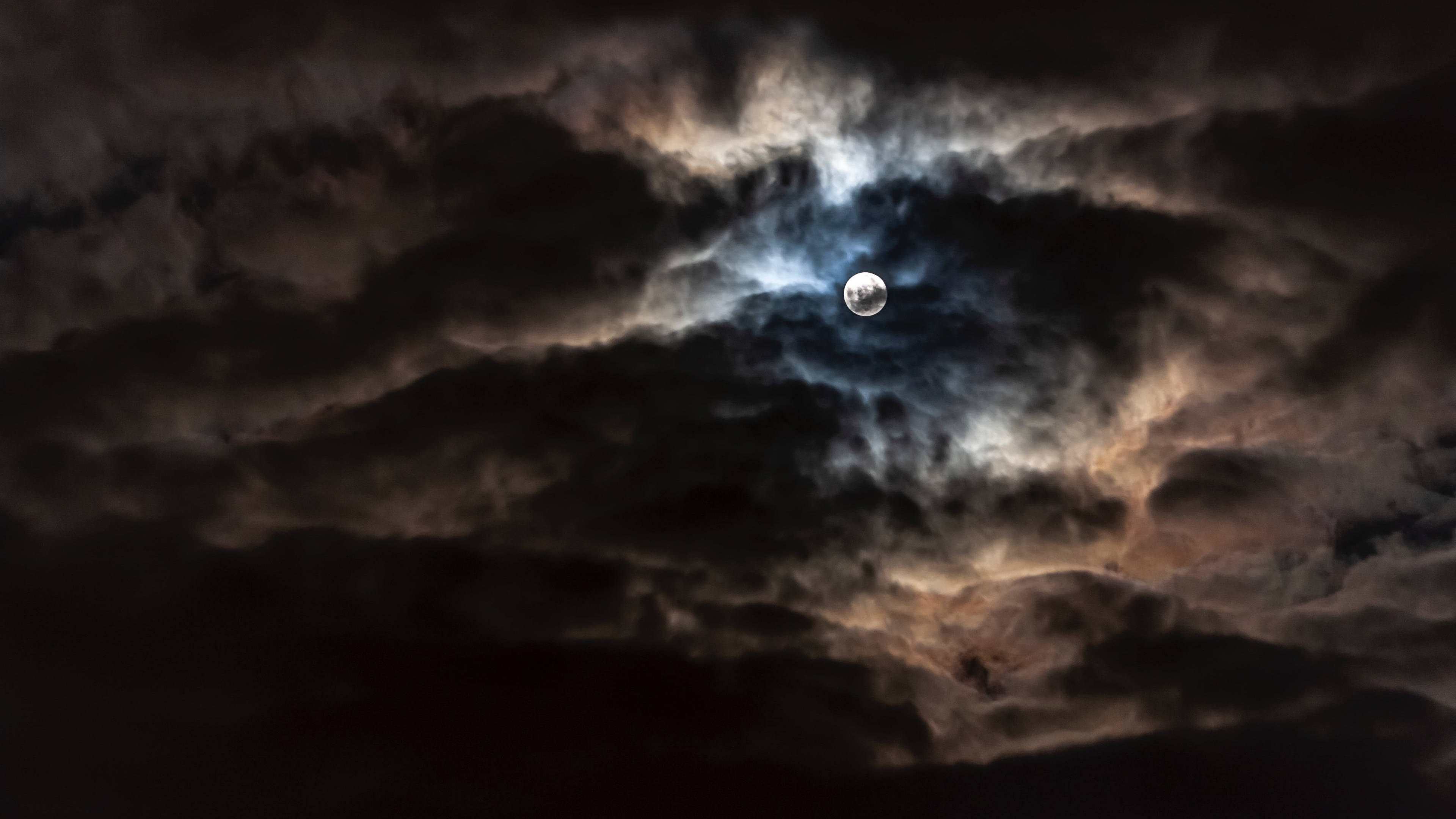陰鬱雲層月光4K 壁紙 — 一輪明亮的月亮穿透戲劇性的烏雲，在夜空中投射出空靈的藍色和橙色光芒。