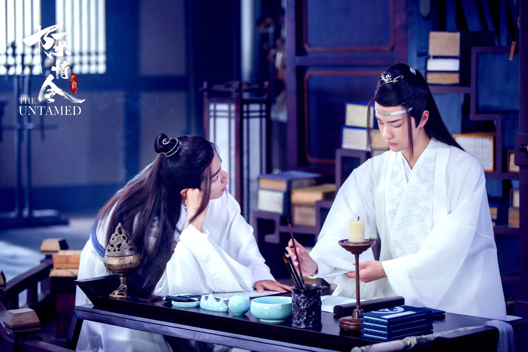 《陳情令》圖書館海報 壁紙 — 兩個身穿白色古袍的人物坐在一張有墨筆和蠟燭的書桌前，房間內有昏暗的藍色燈光。