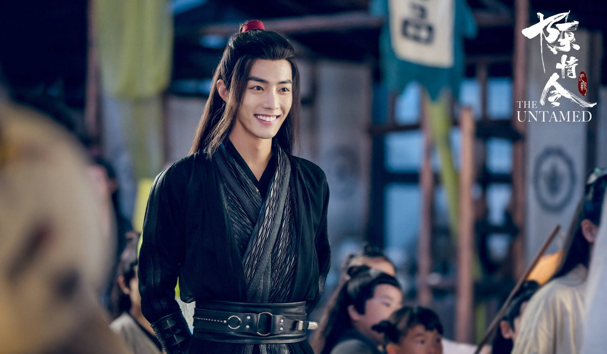 《陳情令》微笑魏嬰 壁紙 — 一位微笑的年輕男子穿著黑色傳統長袍，自信地站在熙熙攘攘的古代中國市場中。