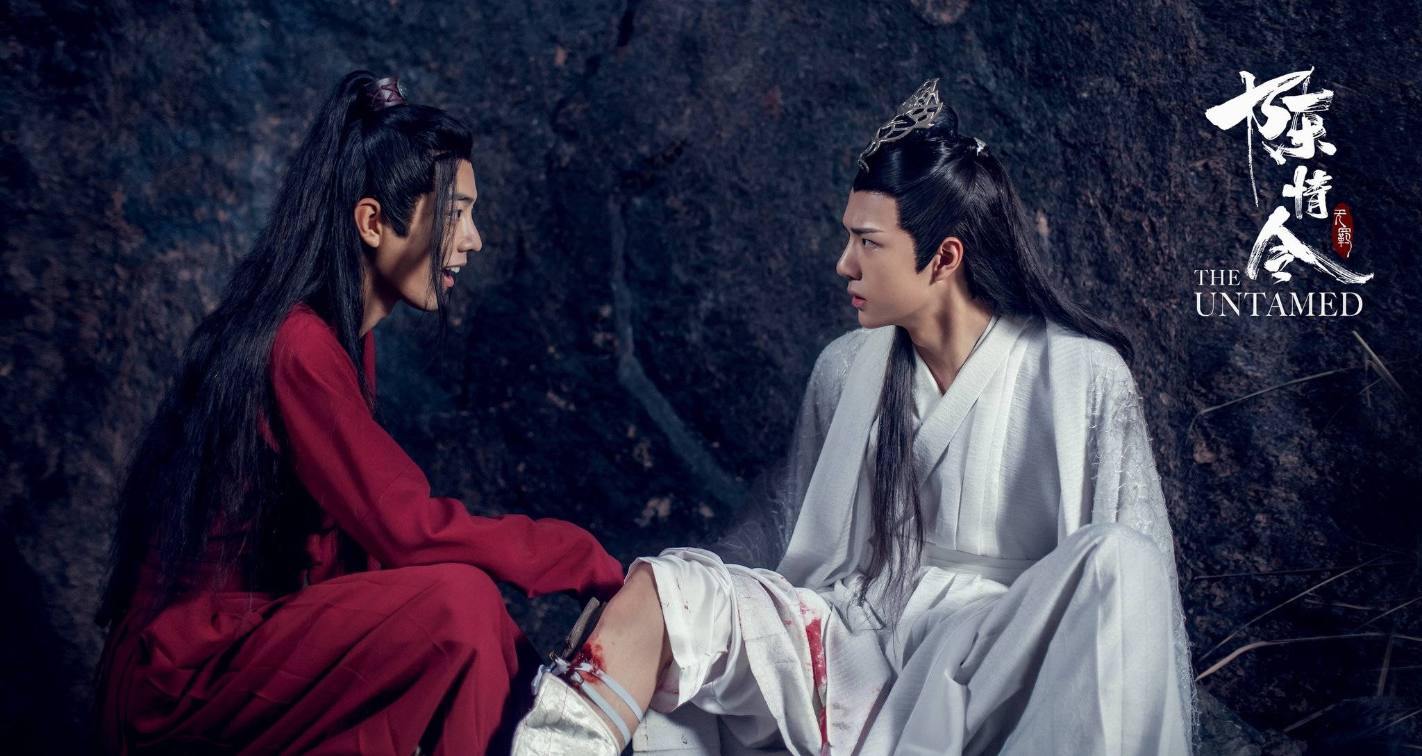 《陳情令》搞笑王權場景 壁紙 — 兩個穿著古裝長袍的男人在黑暗的洞穴中面對面坐著，一個穿紅色，另一個穿白色，腿上帶血。