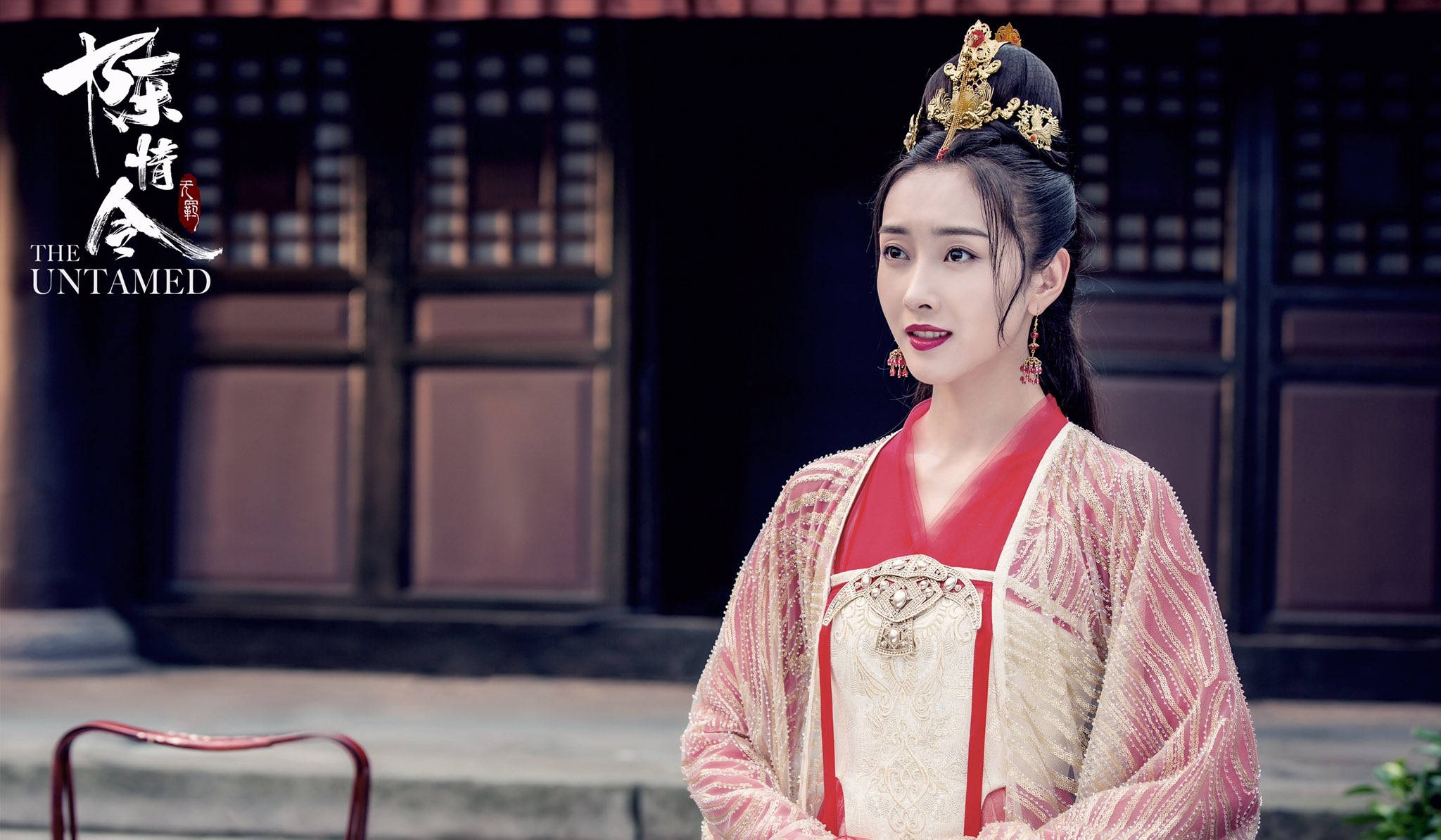 《陳情令》江厌离嫁衣 壁紙 — 一位身穿華麗紅金傳統長袍的女性站在一座帶有精緻格子窗的深色木建築前。