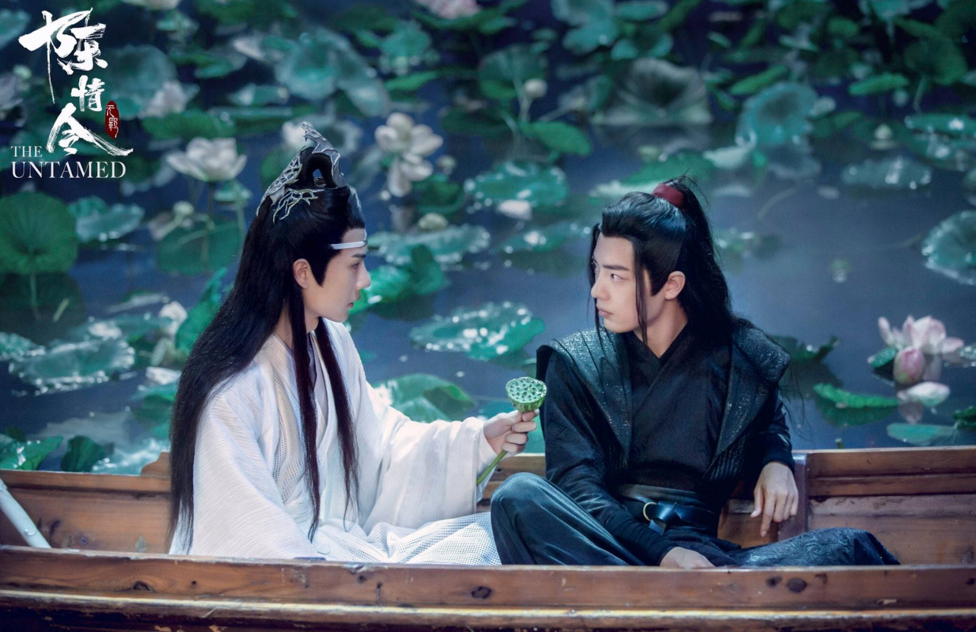 《陳情令》蓮花橋泛舟 壁紙 — 兩個身穿古裝的男人坐在荷花池的木船上，在柔和的暮光下交換一片綠色荷葉。