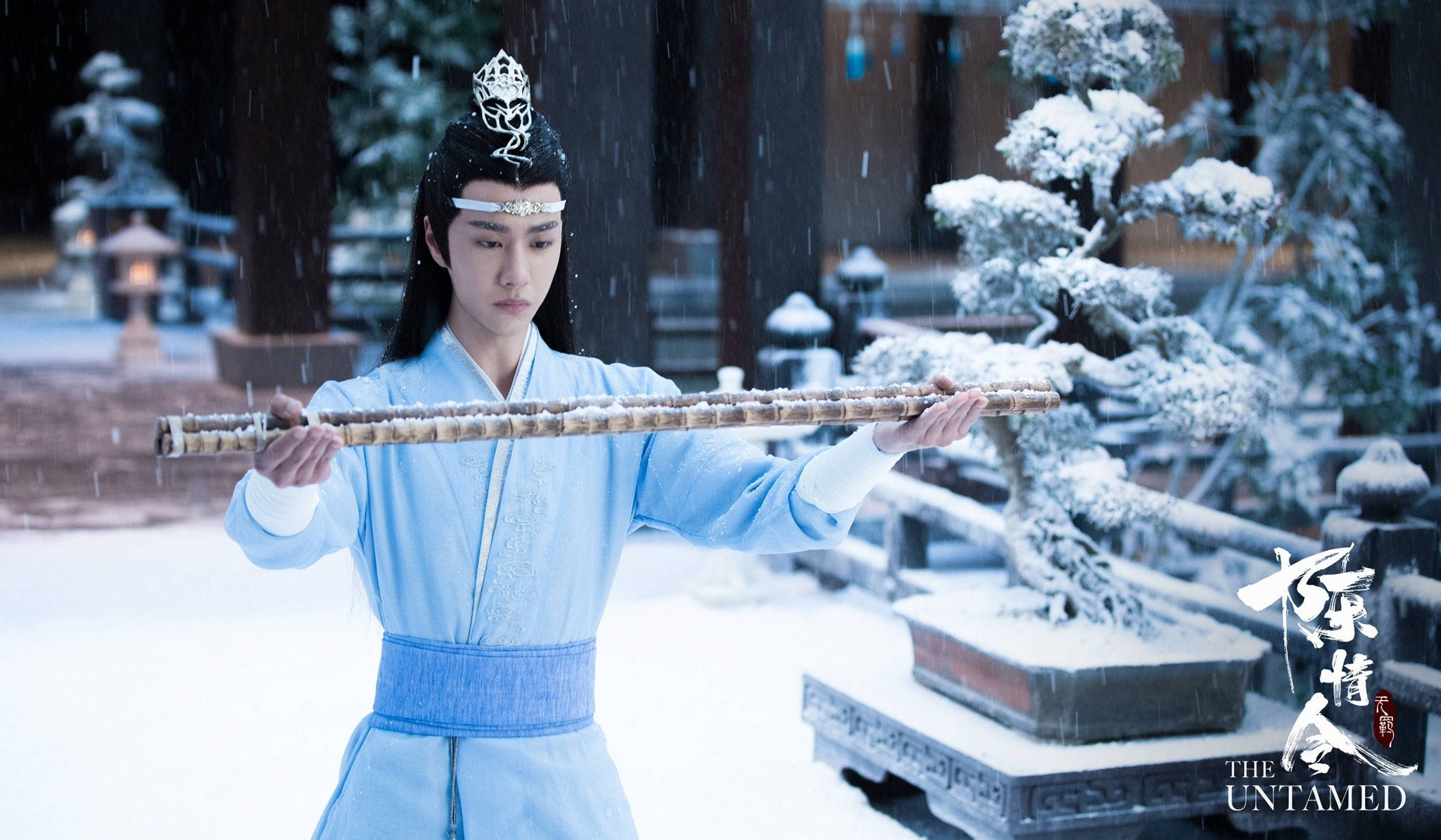 《陳情令》藍忘機受罰 壁紙 — 一位身穿淺藍色傳統長袍的年輕男子，在寧靜的冬日庭院中，手持長竹杖，雪花飄落。
