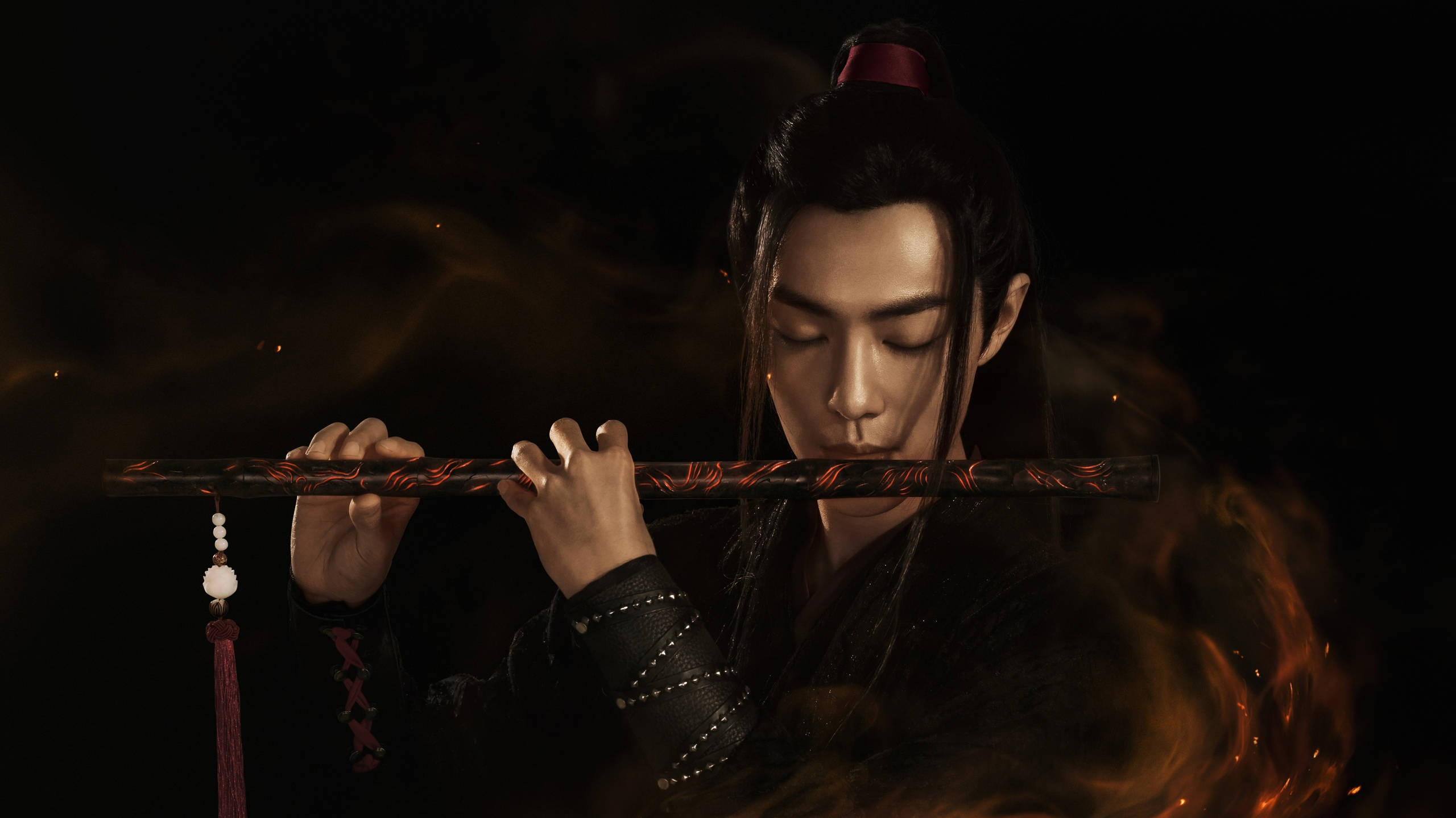 《陳情令》魏無羨吹笛 壁紙 — 一名身穿深色傳統長袍的男子在黑色背景下吹奏長笛，熾熱的橙色火焰在他周圍旋轉。