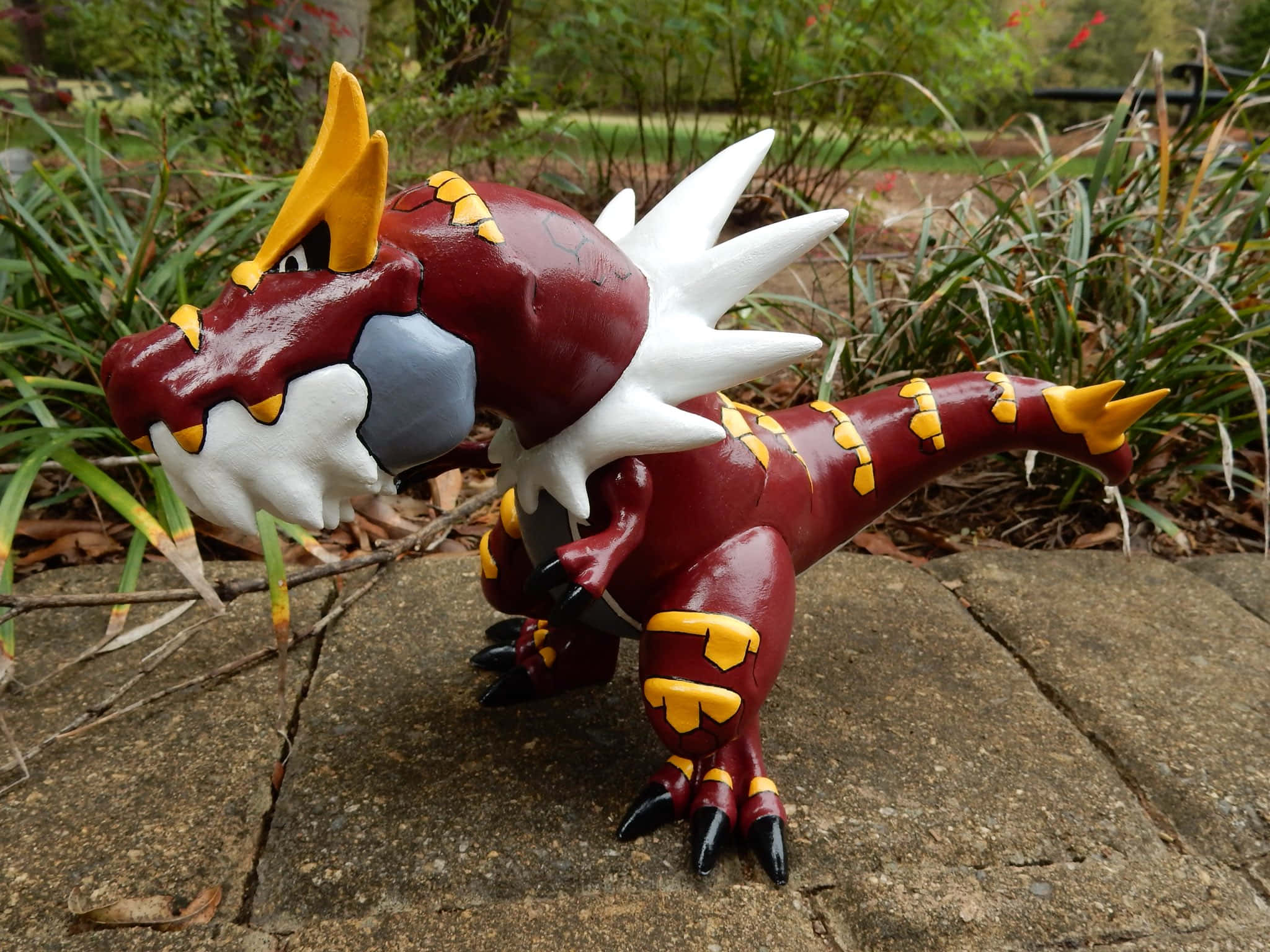 陶瓷 Tyrantrum 壁紙 — 一隻手繪的栗色和黃色龍雕像，帶有白色尖刺，站在石板上，周圍是綠色植物。