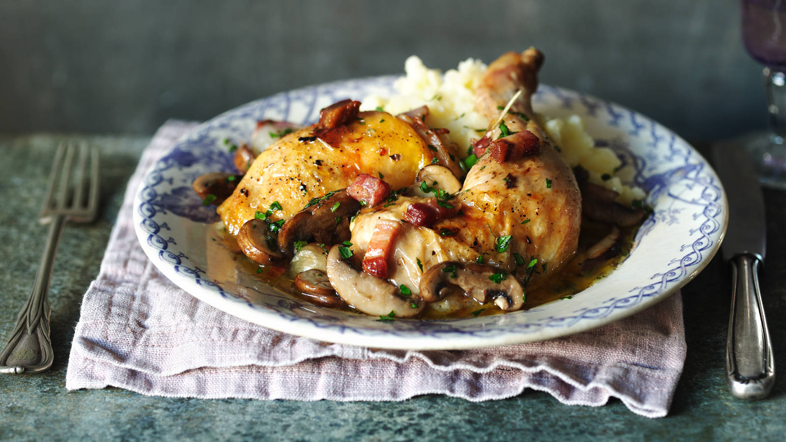 陶瓷盤上的誘人Coq Au Vin 壁紙 — 金黃色烤雞配蘑菇和煙肉，放在藍色圖案碟上，伴以薯蓉。