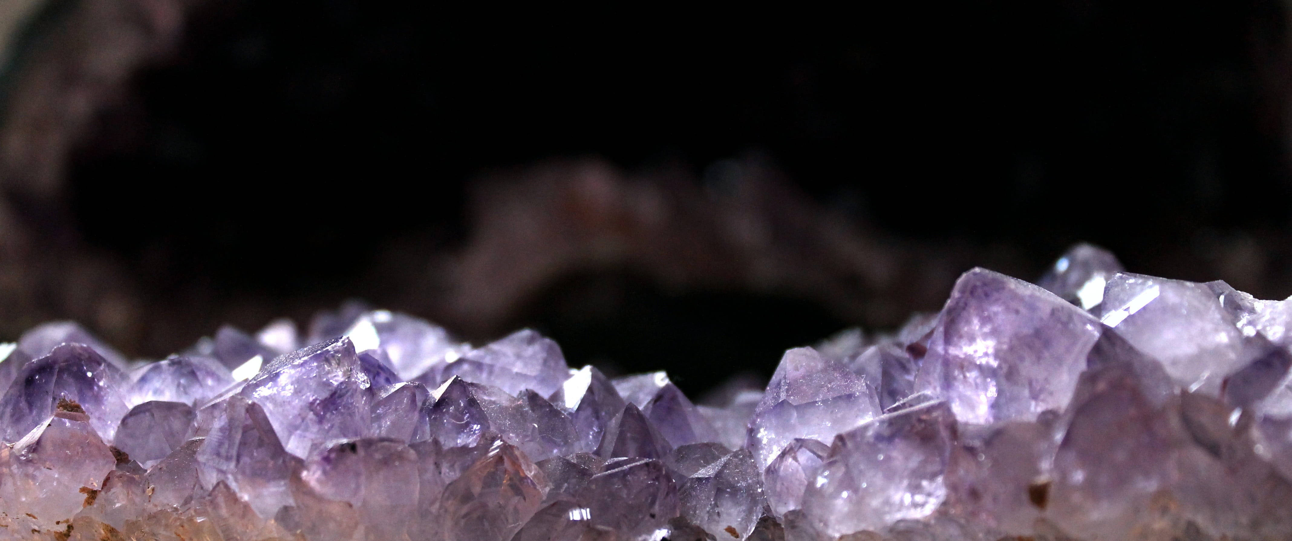 陽光下的鋒利紫水晶 壁紙 — 閃爍紫色紫水晶晶體在黑暗洞穴背景中發光的特寫。