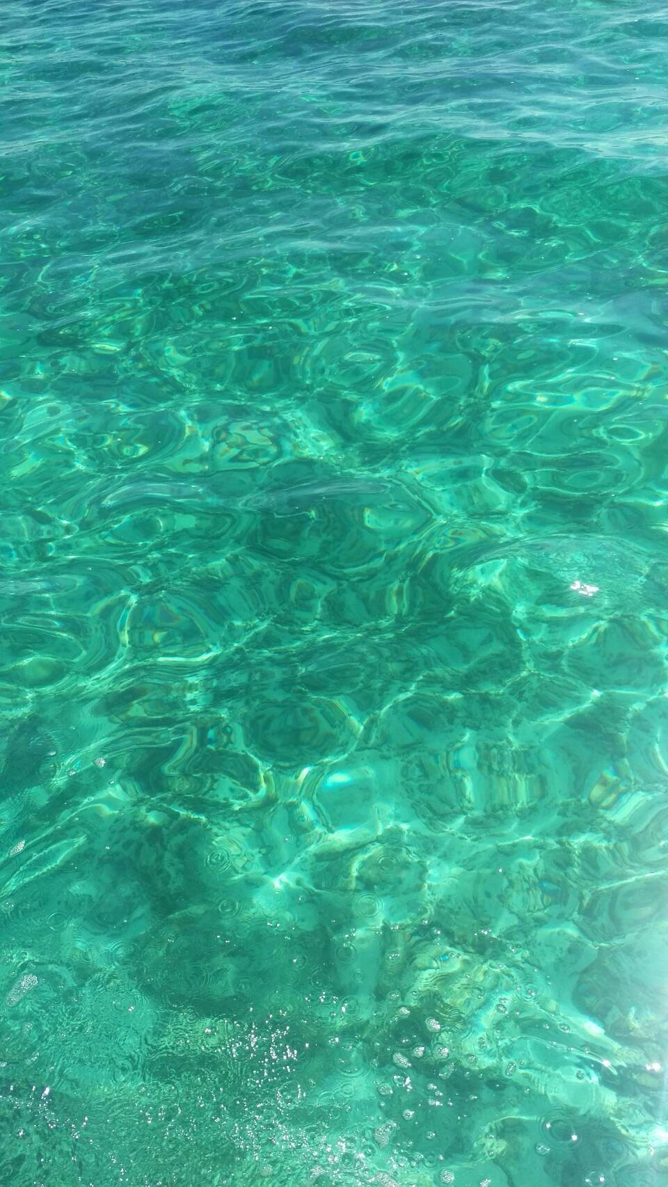海洋 桌布 壁紙 — 陽光在清澈的碧綠海面上舞動，顯露出溫柔漣漪下的岩石海床。