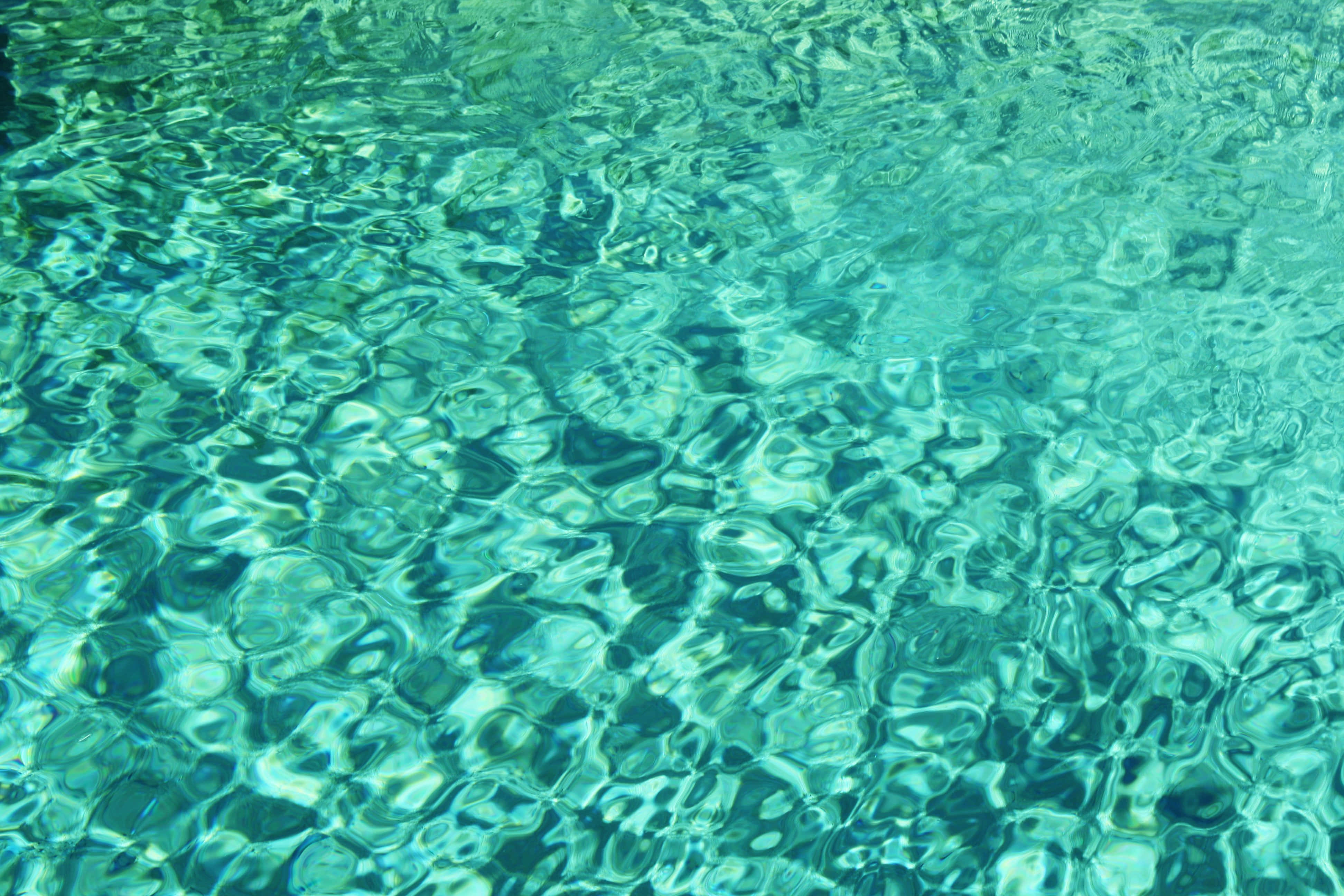 Turquoise Blue 桌布 壁紙 — 陽光在漣漪的碧綠水面上舞動，顯露出水面下清晰的岩石。