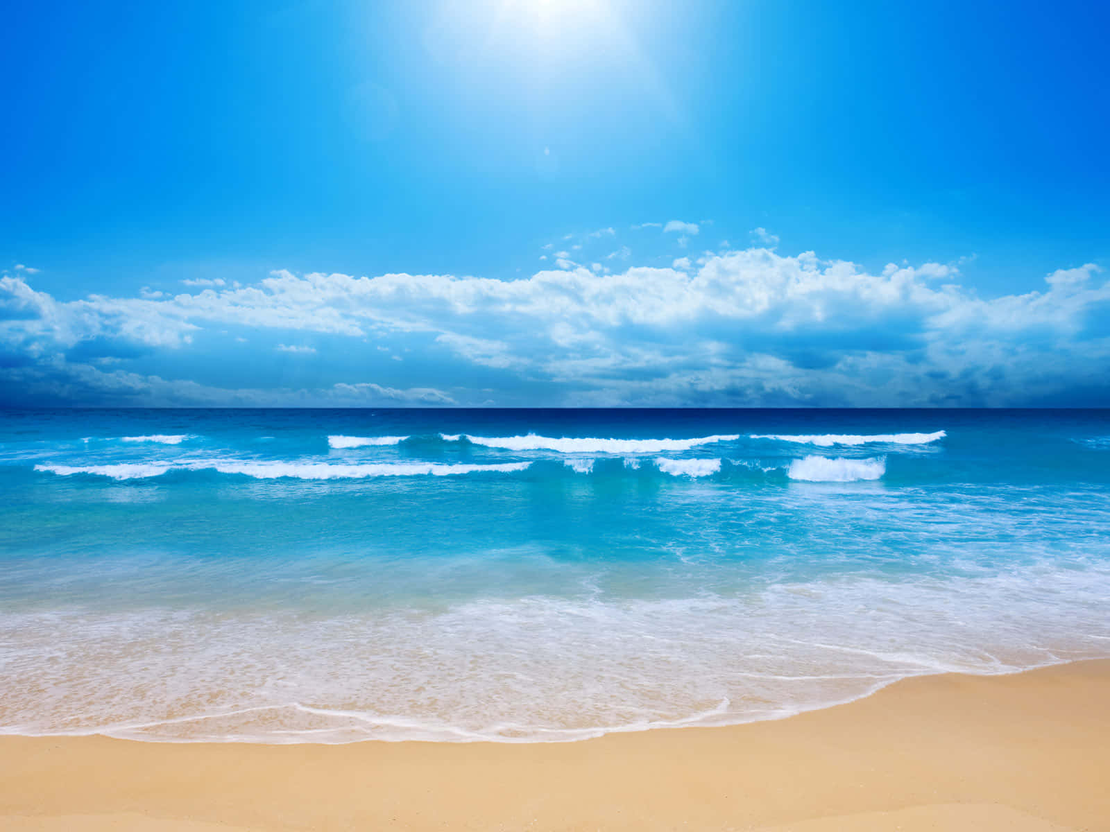 Seashore 桌布 壁紙 — 陽光在碧綠色的海洋上閃耀，翻滾的海浪沖刷著金色的沙灘，天空湛藍，白雲蓬鬆。