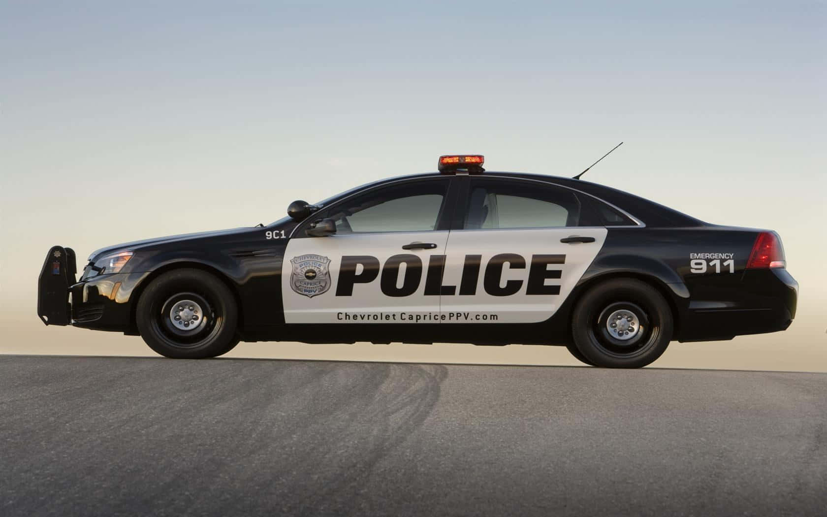 陽光明媚日的強勁警車 壁紙 — 一輛黑白警車帶有 'POLICE' 和 'EMERGENCY 911' 標記，停在晴朗天空下的瀝青路面上。