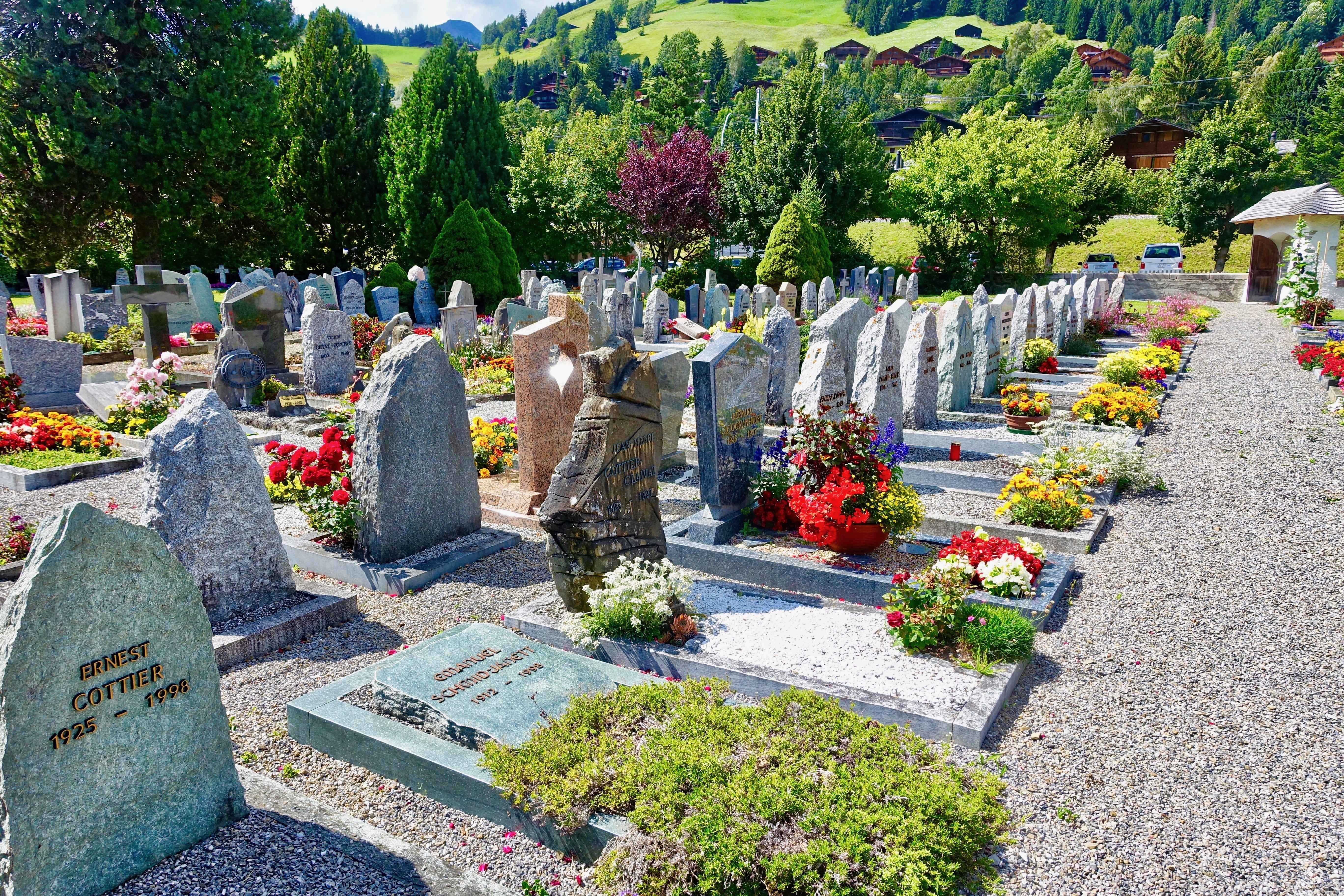 Gravestone 桌布 壁紙 — 陽光明媚的墓地，石墓上點綴著鮮豔的紅、黃、白花朵， nestled among green trees and hills.