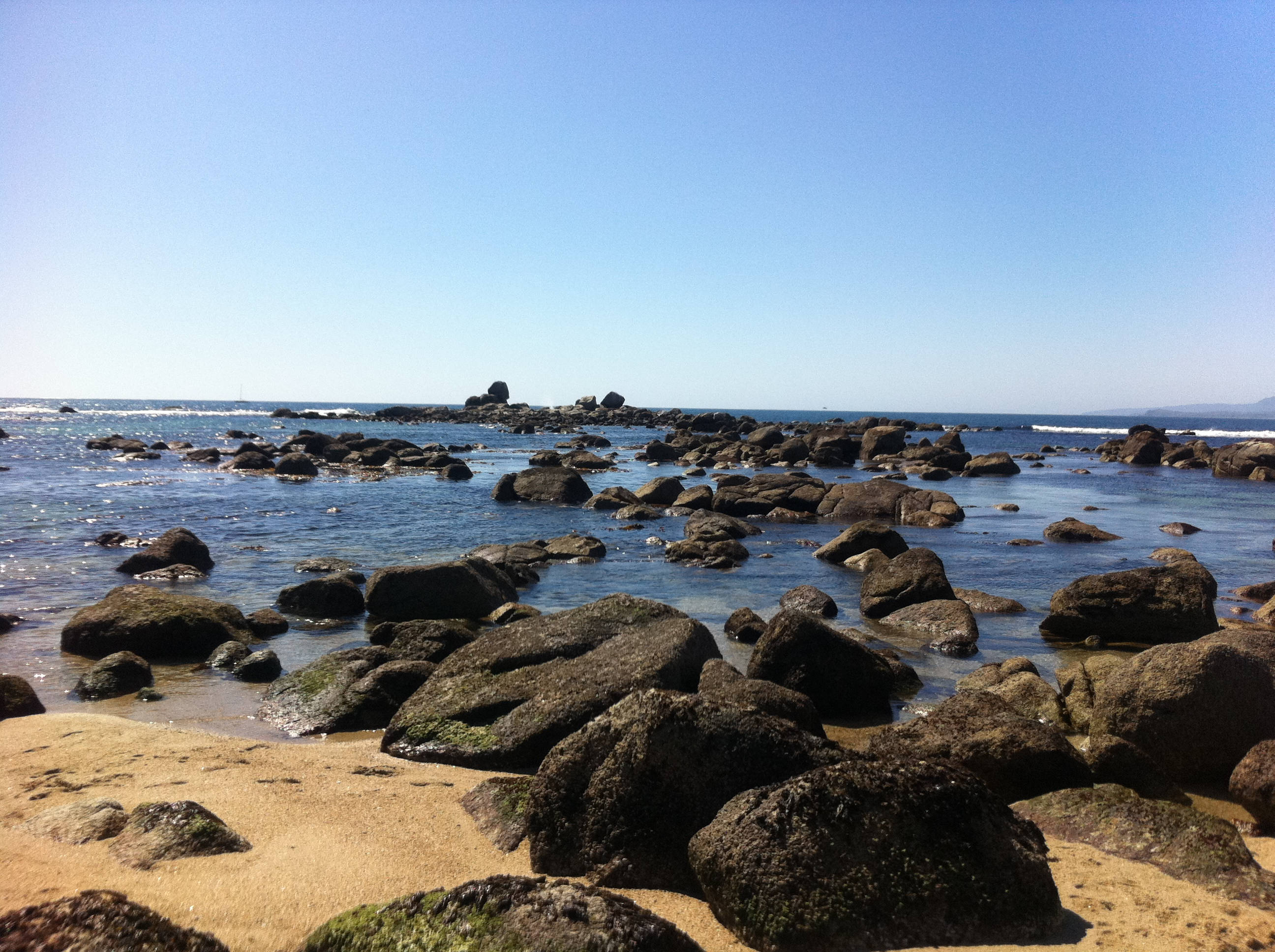 Beach Desktop 桌布 壁紙 — 陽光明媚的海灘，有深色岩石和淺綠松石色的海水，在清澈的藍天下。