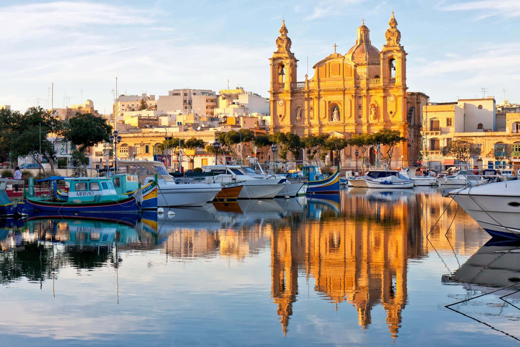 Malta 桌布 壁紙 — 陽光明媚的港口，色彩繽紛的船隻和宏偉的金色教堂在金色時刻倒映在平靜的水面上。