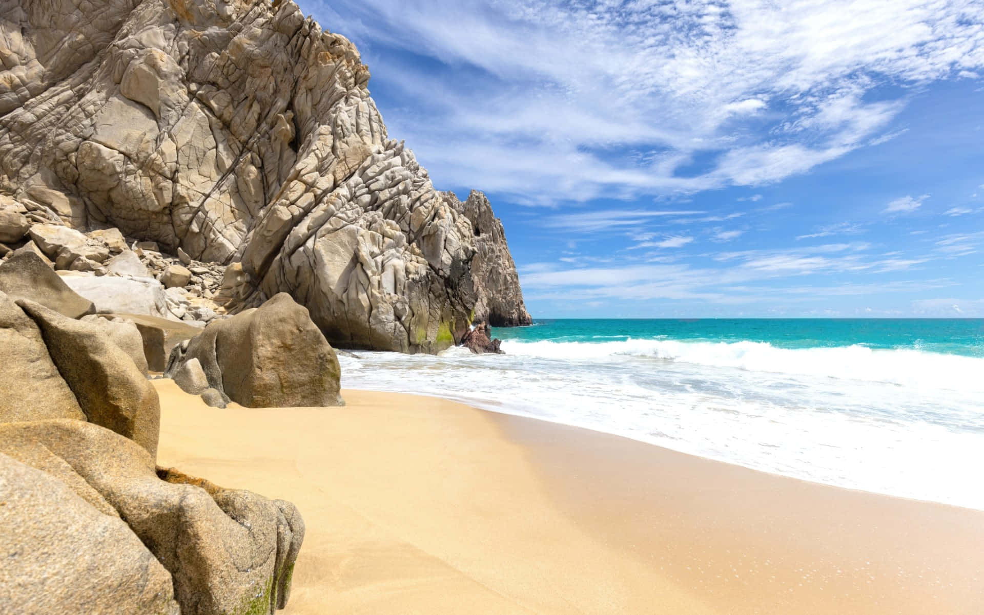 Mexican Beach 桌布 壁紙 — 陽光普照的海灘，金色沙灘與碧綠色的海浪拍打高聳的岩石懸崖，天空湛藍明亮。