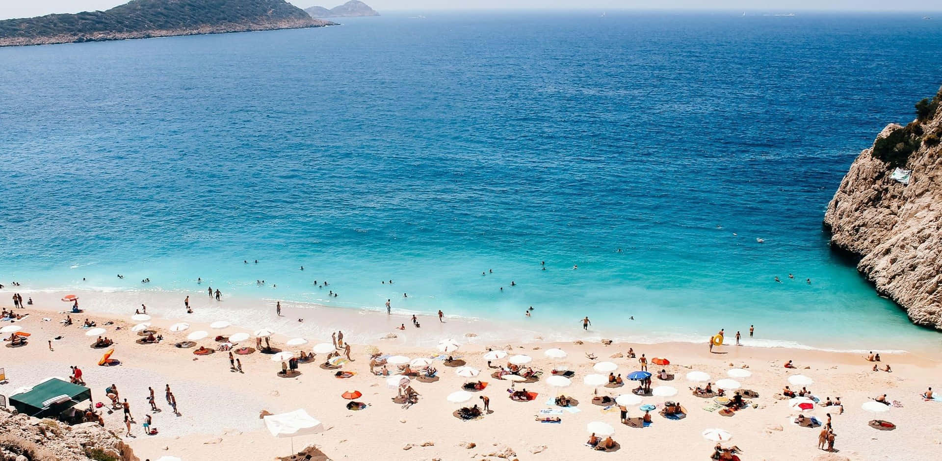 Mediterranean Beach 桌布 壁紙 — 陽光普照的海灘鳥瞰圖，碧綠海水，人群聚集在白色遮陽傘下。