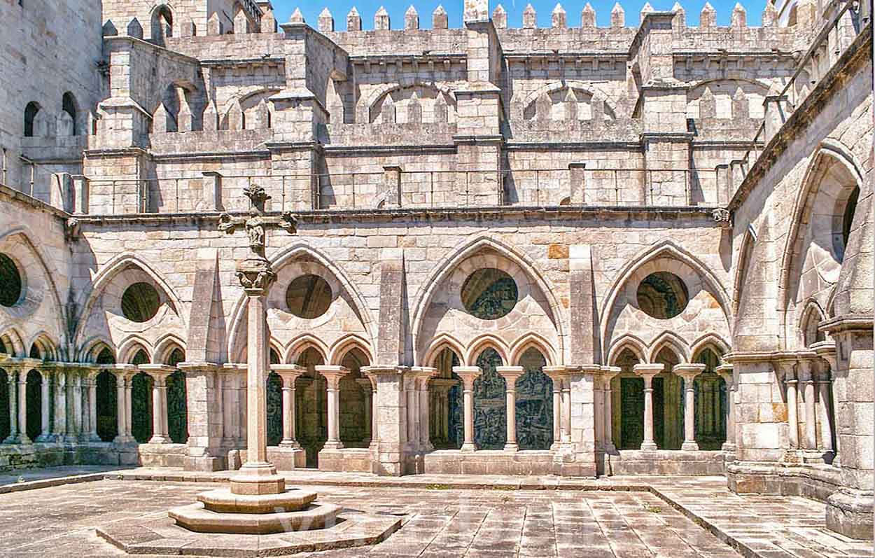 Gothic Architecture 桌布 壁紙 — 陽光普照的石頭迴廊，有拱形步道和中央十字架，在清澈的藍天下。