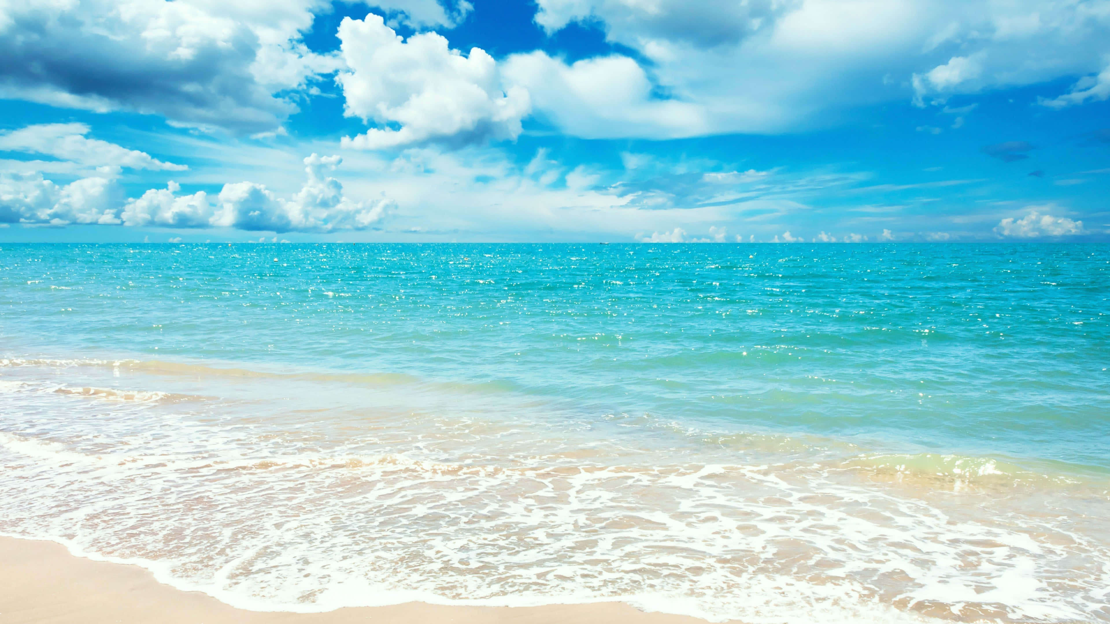 Beach Holiday 桌布 壁紙 — 陽光普照的碧綠海浪輕輕拍打著金色沙灘，上方是點綴著蓬鬆白雲的湛藍天空。