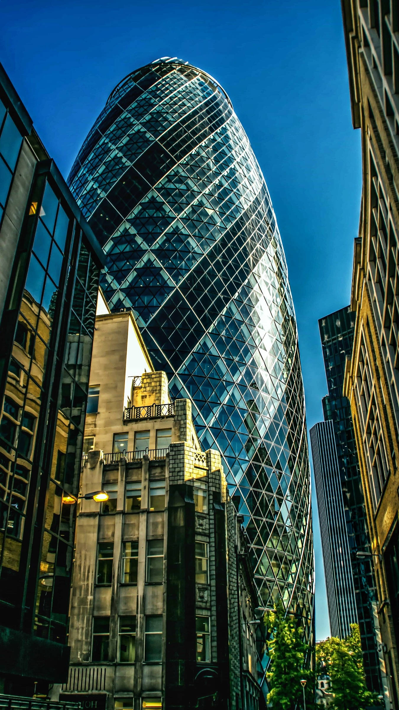 陽光灑在The Gherkin上 壁紙 — 倫敦標誌性小黃瓜摩天大樓的低角度景觀，其玻璃外牆反射著清澈的藍天。