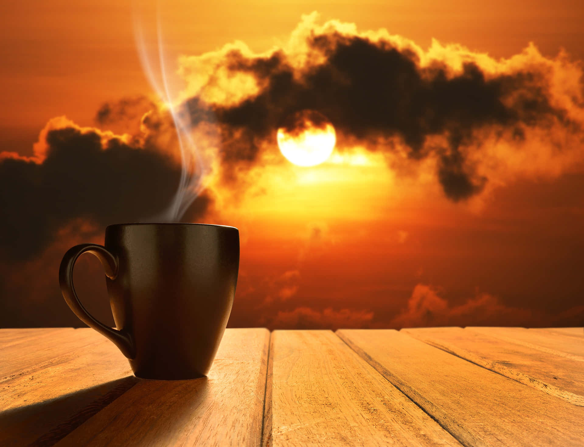日落時木桌上的熱咖啡杯與橙色雲彩