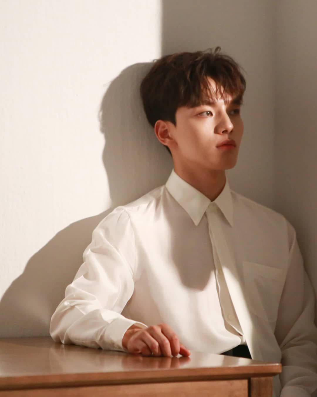 陽光灑落的 Yeo Jin Goo 壁紙 — 一位身穿筆挺白襯衫的年輕男子靠在牆上，柔和陽光在他臉上和木桌上投下戲劇性的陰影。