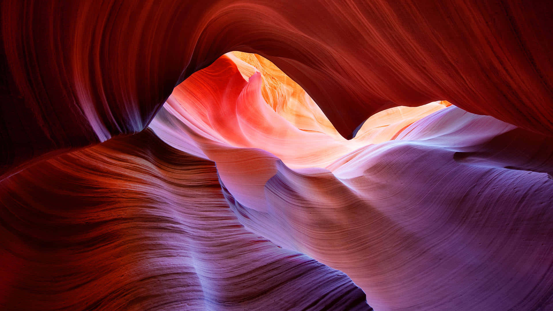 macOS 桌布 壁紙 — 陽光照亮狹窄峽谷中旋轉的紅色、橙色和紫色砂岩波紋。