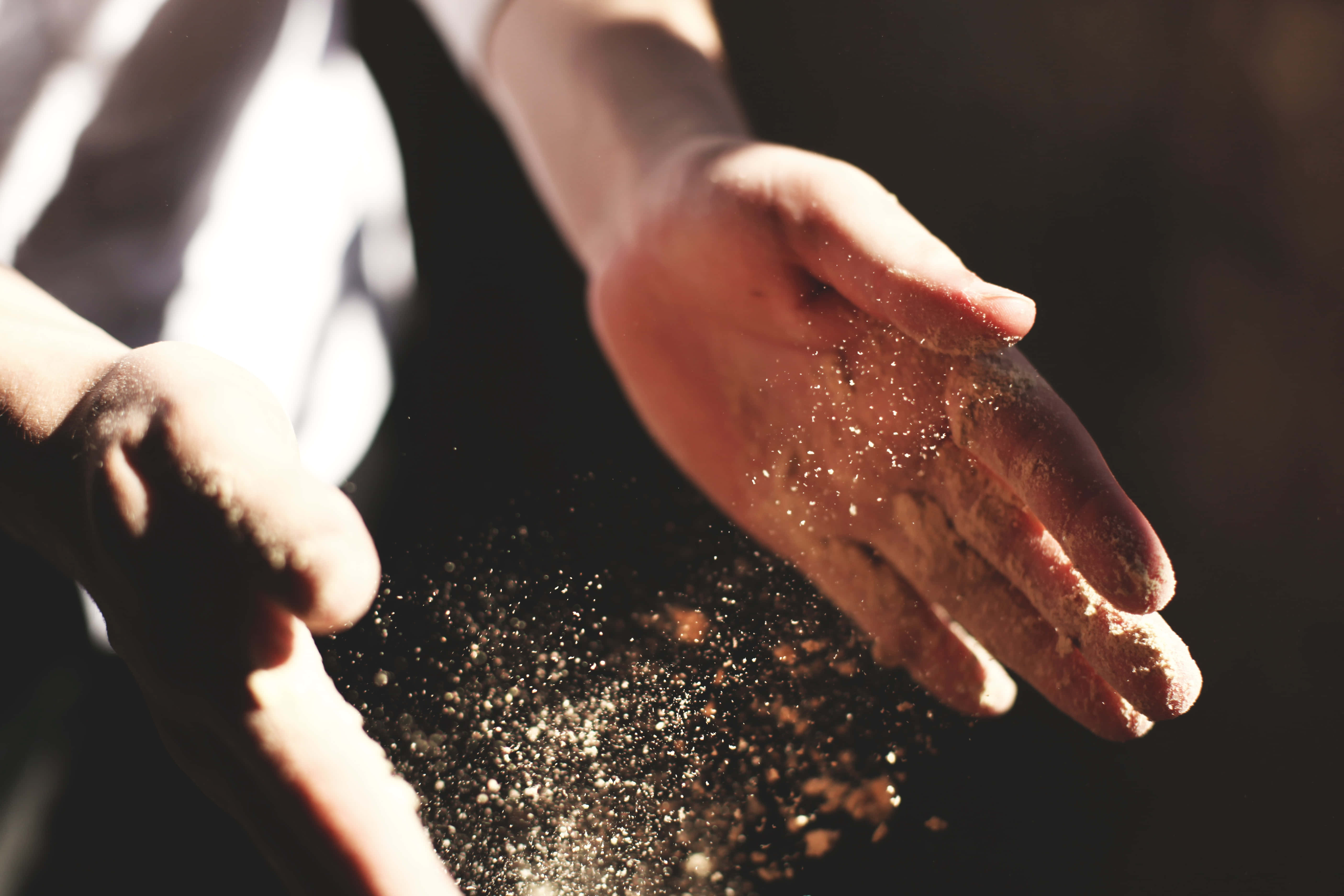 Dust 桌布 壁紙 — 陽光照射下的雙手，在黑暗背景中輕輕釋放出一連串金色塵埃粒子。