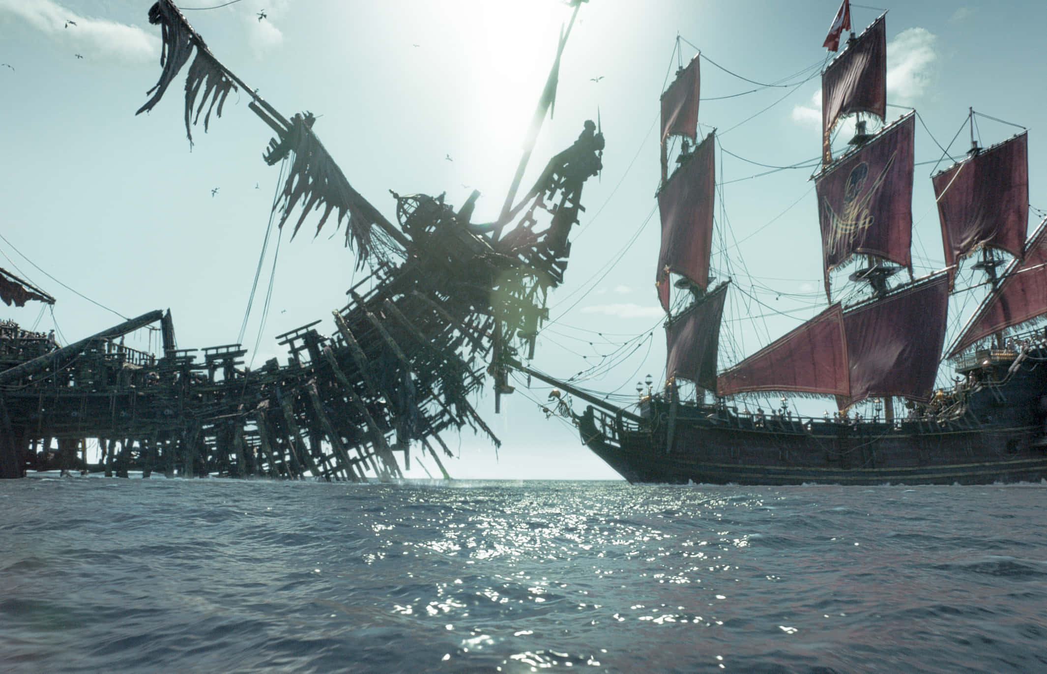 Pirate Ship 桌布 壁紙 — 陽光照耀的海景，一艘失事船隻傾斜入水，旁邊是一艘完好無損、掛著紅帆的帆船。