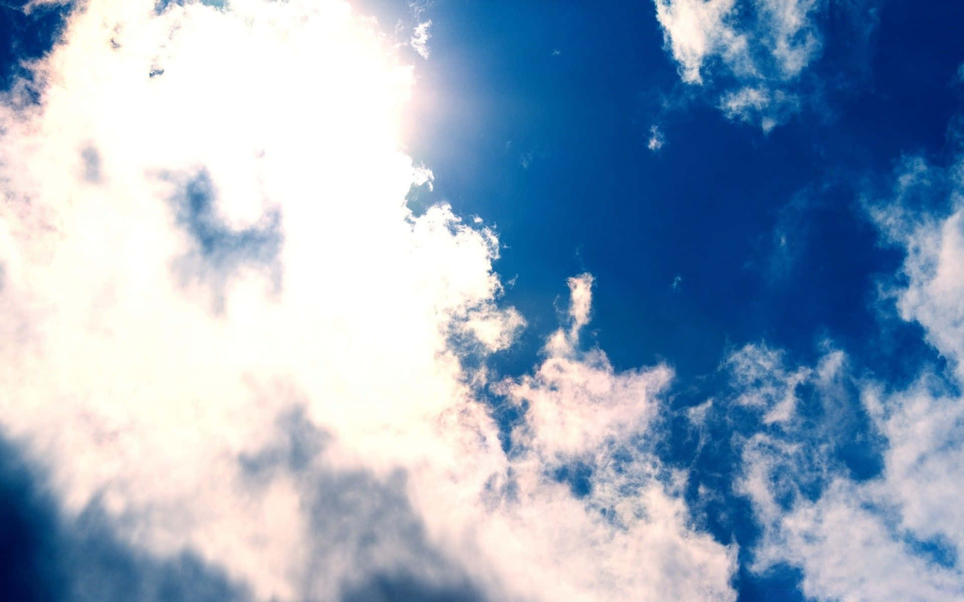 Spring Sky 桌布 壁紙 — 陽光穿透蓬鬆的白雲，映襯著充滿活力的藍天，呈現動態的俯拍畫面。