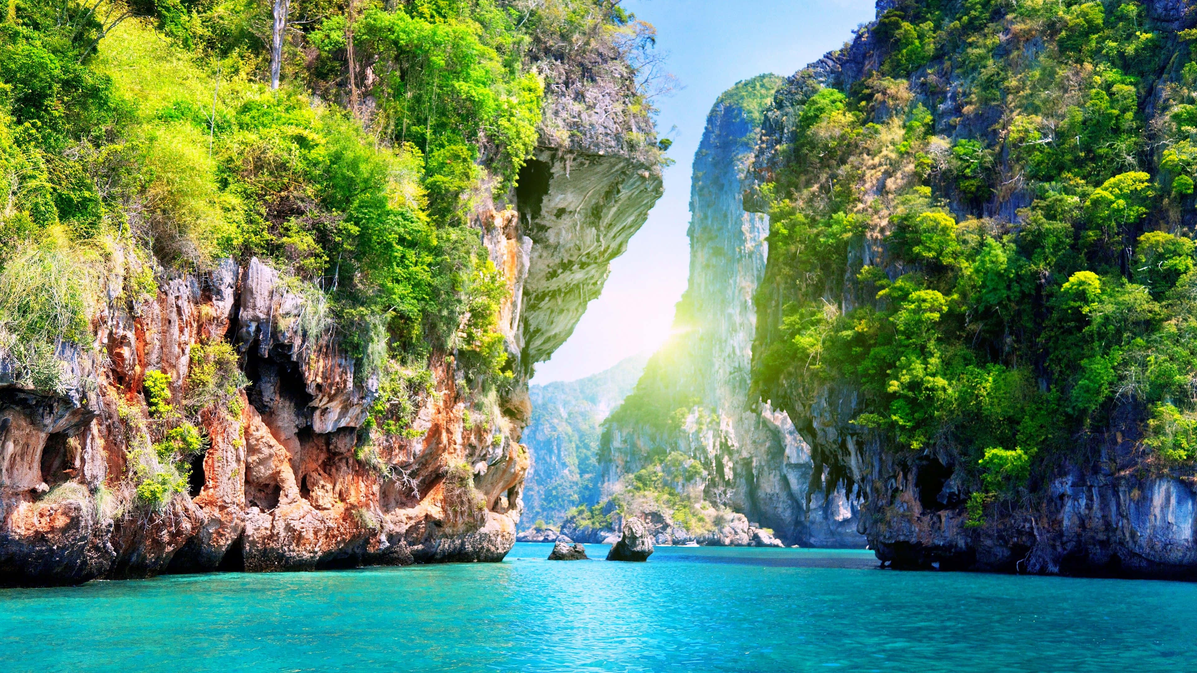 Thailand Beach 桌布 壁紙 — 陽光穿過天然岩石拱門，照射在碧綠海水上，四周環繞著鬱鬱蔥蔥的綠色懸崖。