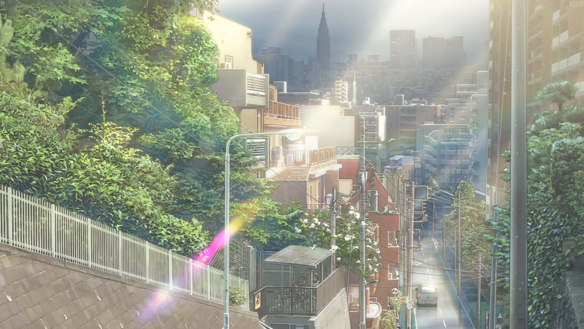 Weathering With You 桌布 壁紙 — 陽光穿過茂密的綠色山坡，俯瞰著一個密集的城市社區，遠處有摩天大樓。