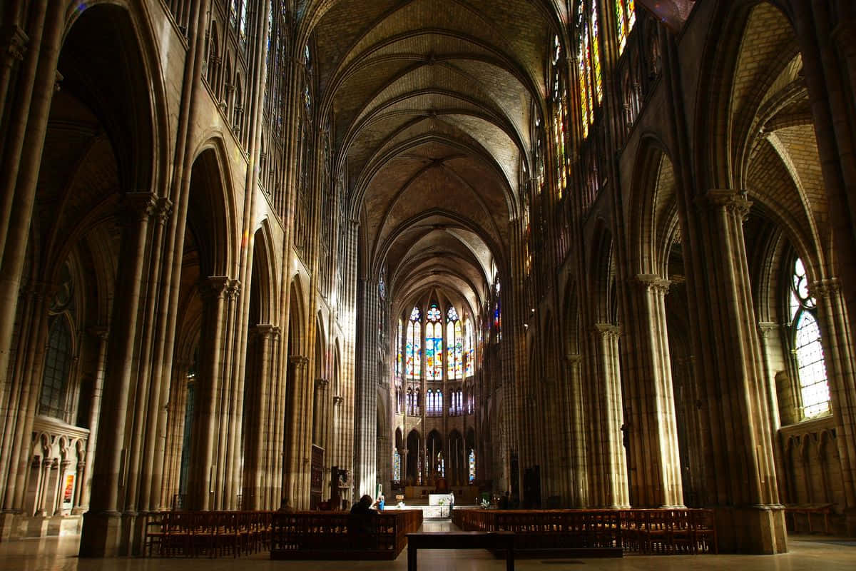 Gothic Architecture 桌布 壁紙 — 陽光透過彩繪玻璃窗照射進來，照亮了大教堂內部高聳的石拱門和木製長椅。